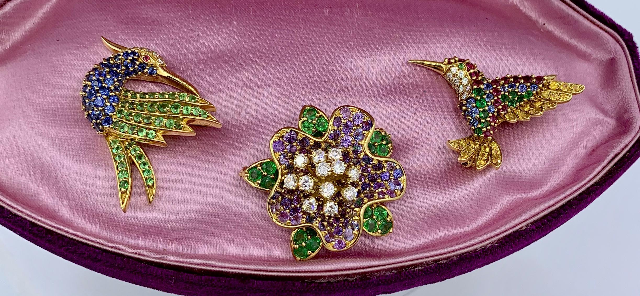 This is a trio of three signed Jean Vitau Brooch Pins with a Flower and two Birds, Hummingbird, set with Sapphires, Diamonds, Tsavorite Green Garnets, Yellow Sapphires, Rubies, and Purple Sapphires and in 18 Karat Gold.
The three jewels by the famed