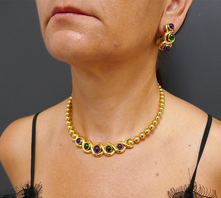 A vintage Jean Vitau 18k gold set comprises of a necklace and earrings. The set features cabochon amethyst and garnet.
The necklace is comprised of graduated gold beads strung on a gold wire which is only visible from the back. The wire holds five