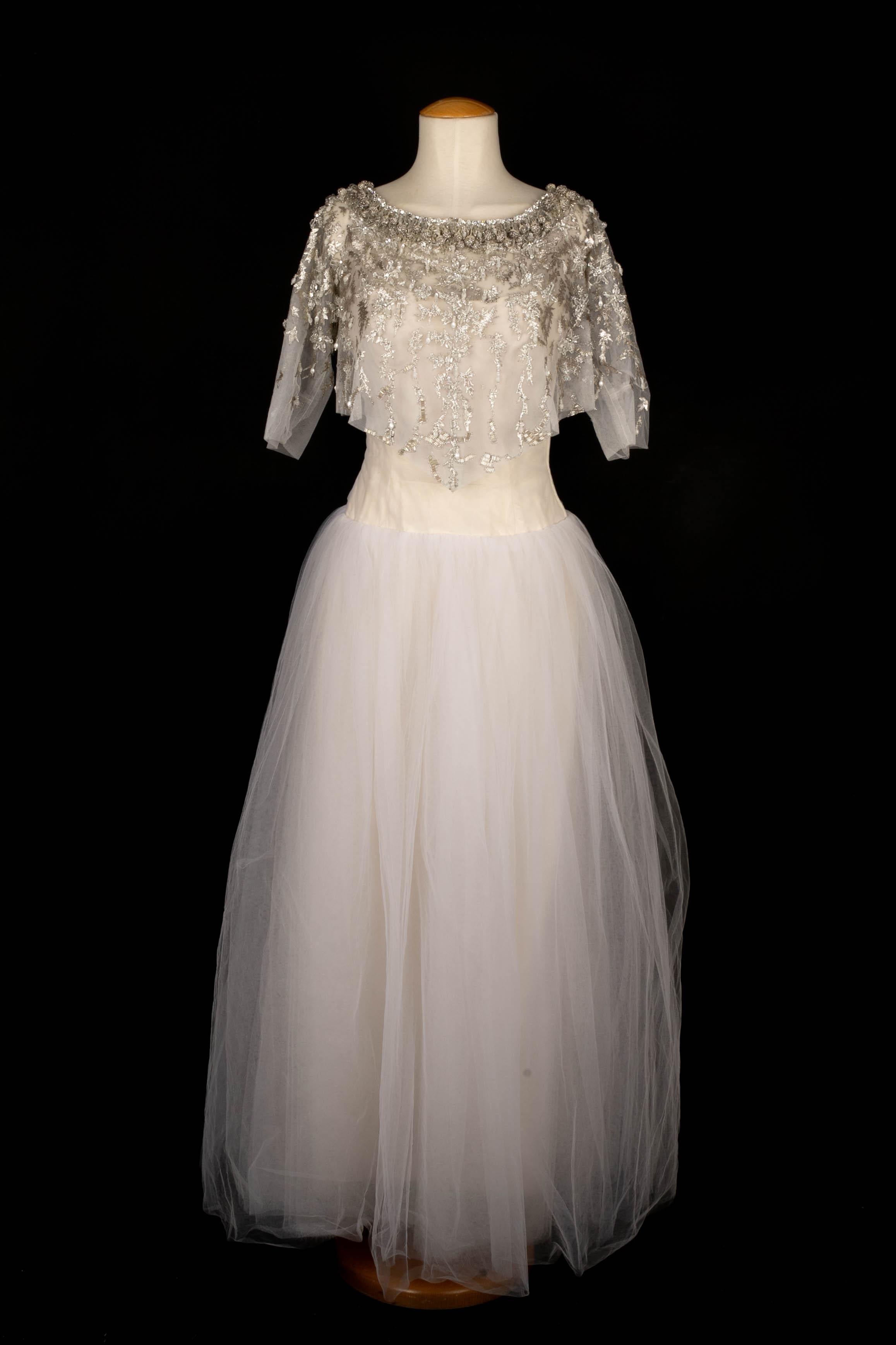 LANVIN -Vestido largo bustier de tul blanco. El corpiño tiene un forro de seda color crema y está deshuesado. El vestido se diseñó con un bolero no firmado hecho de hilos plateados, perlas y pequeños pompones que creaban motivos florales. Sin