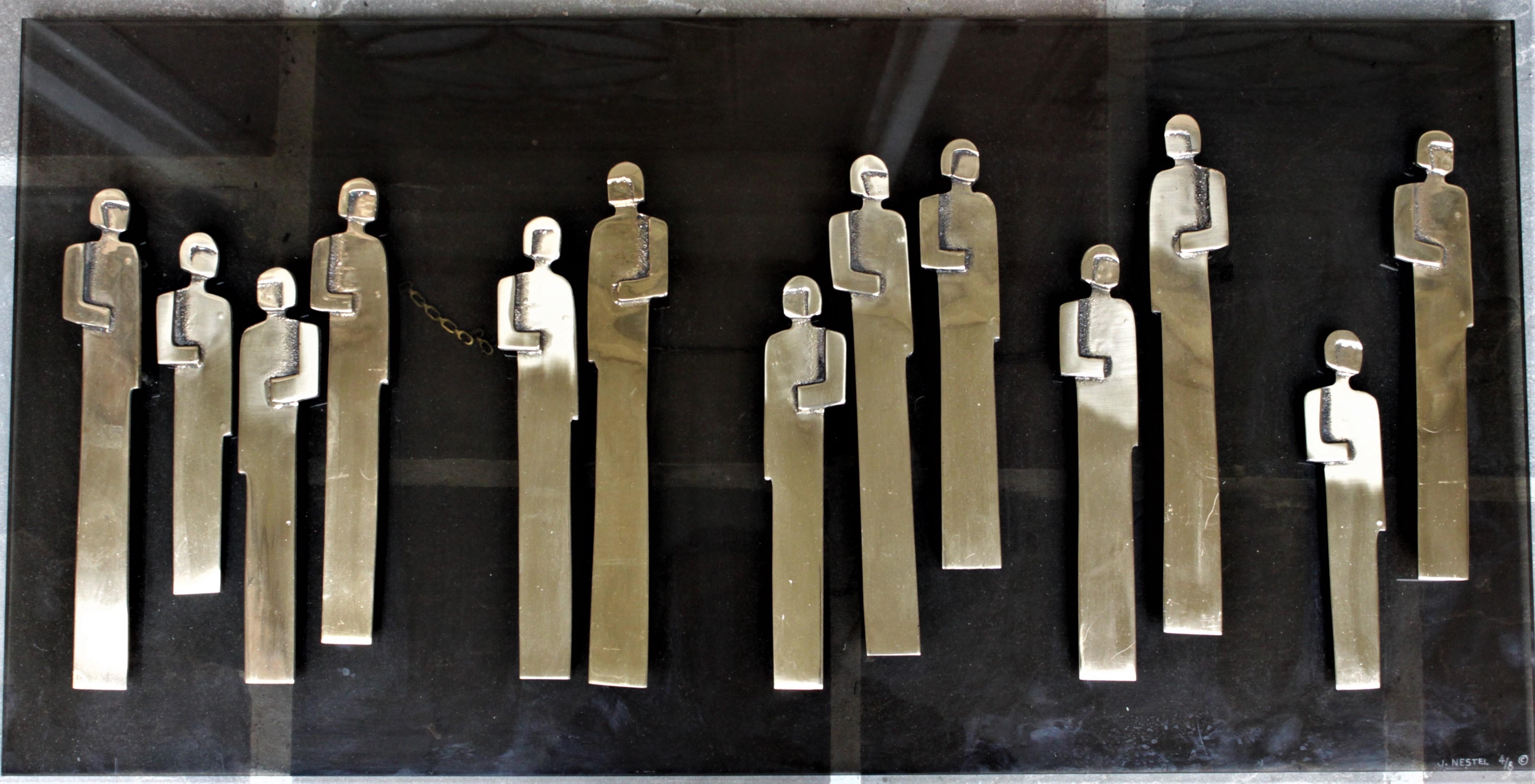 This Lucite and brass wall sculpture is not dated, but presumed to have been made in approximately the 1970s by Canadian artist, Jeannette Nestel. The sculpture features several stylized people done in brass, which are mounted to a thick piece of