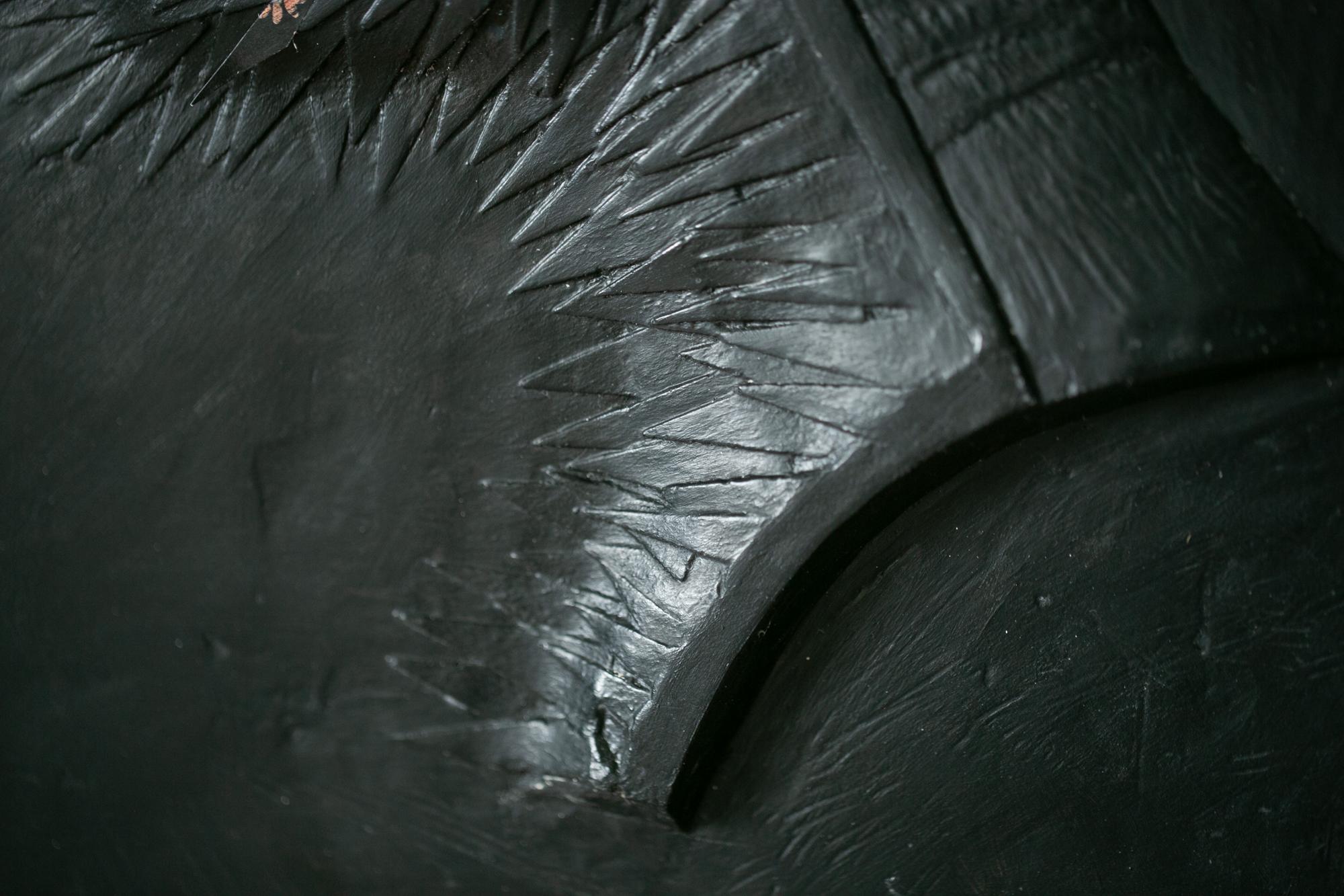 This black, figurative wall-hanging sculpture titled 