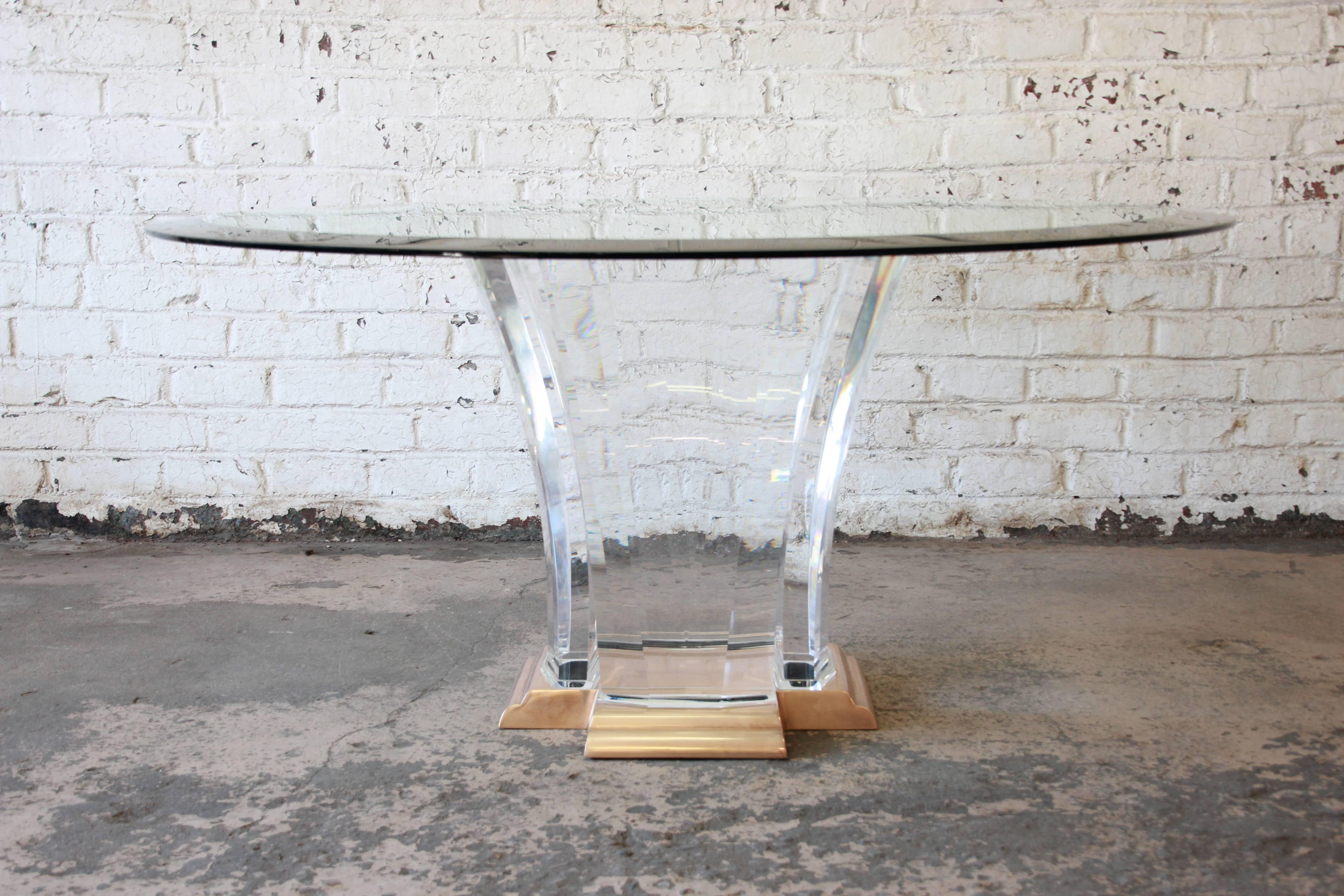 A rare and outstanding sculptural Art Deco inspired dining table designed by Jeffrey Bigelow. A scrolled cast-brass plateau anchors four gently arched, faceted cast-Lucite slab pedestals. The 60