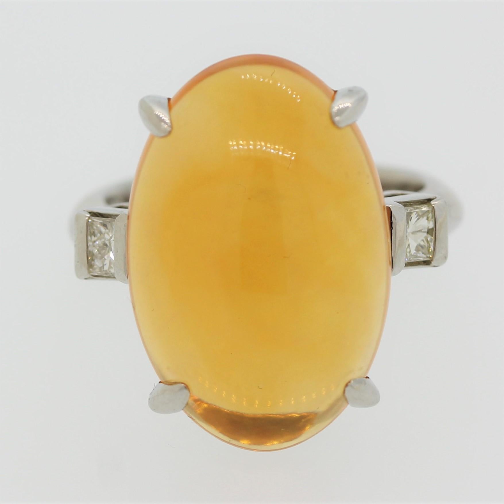 A luscious fire opal weighing 10.95 carats takes center stage. It has a vibrant orange hue with play of color, showing soft flashes of green. It is accented by 2 princess cut diamonds on its shoulders weighing a total of 0.32 carats. Hand fabricated