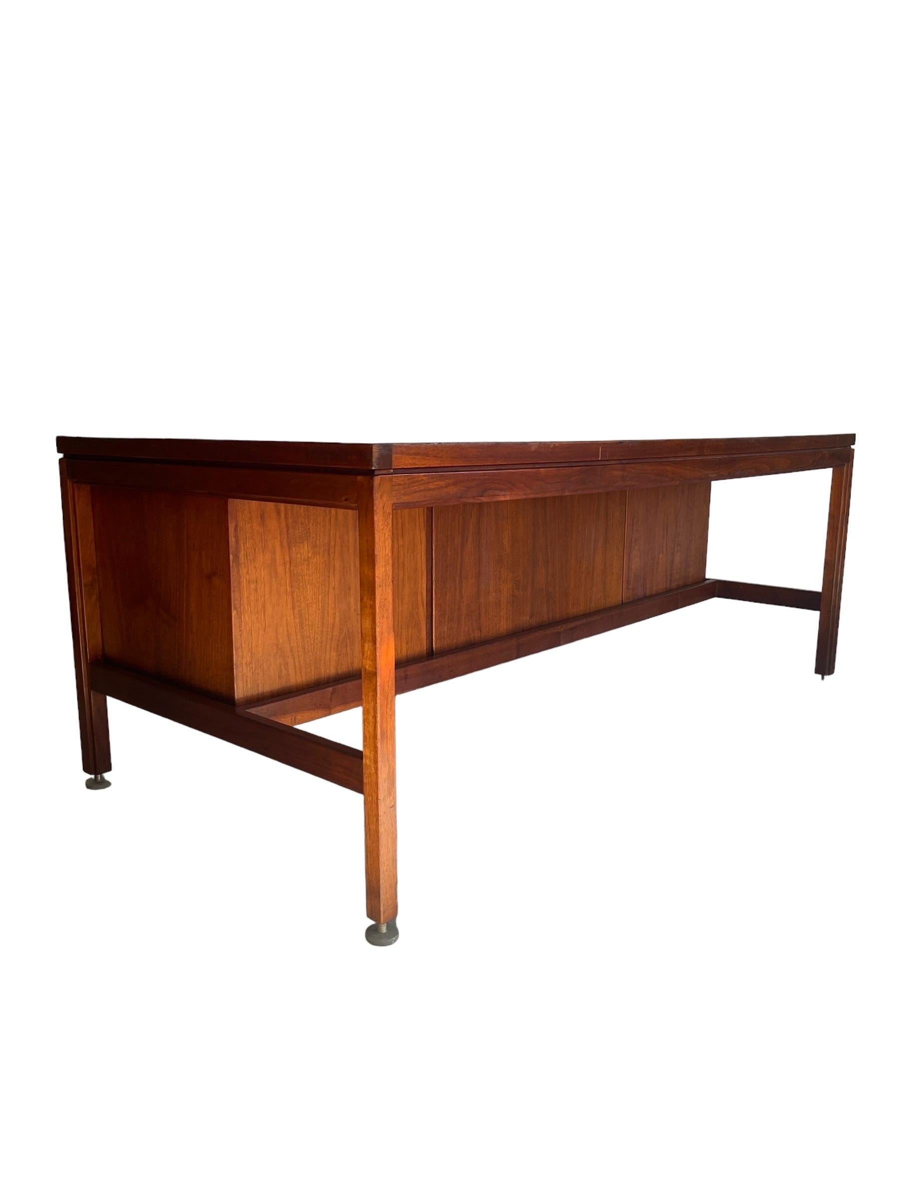 American walnut executive desk design by Jens Risom with four drawers on the right, one drawer in the middle, & one drawer and a filing drawer on the left. Both sides have writing pull-out slides. This desk is in original vintage condition. 

W