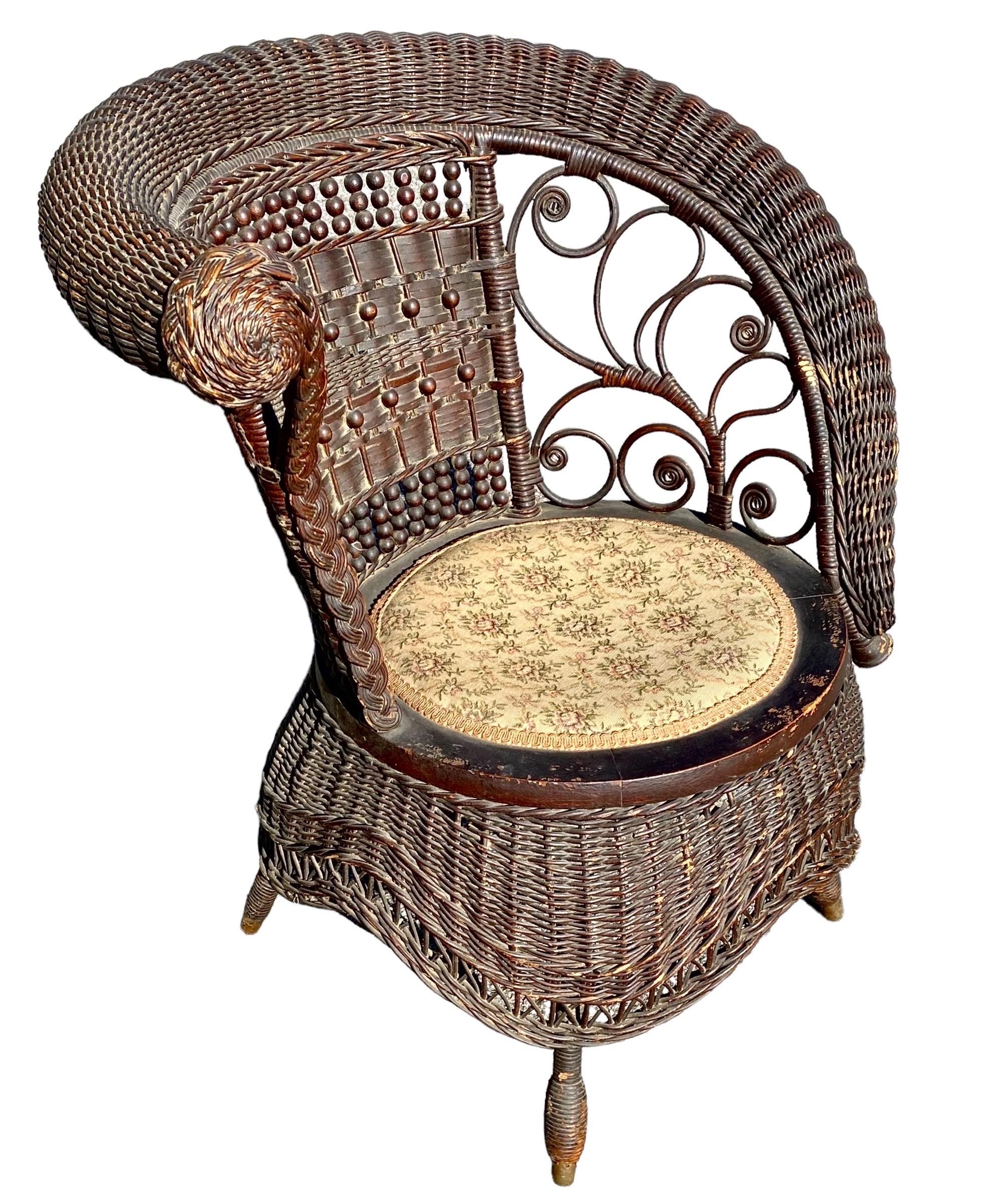Jenkins & Phipps stick and ball wicker photographers or portrait chair with asymmetrical scrolled right arm and fiddleheads, woven skirt, and woven beaded front legs.  Jenkins-Phipps label on underside, dating this chair from between 1903 and 1918.
