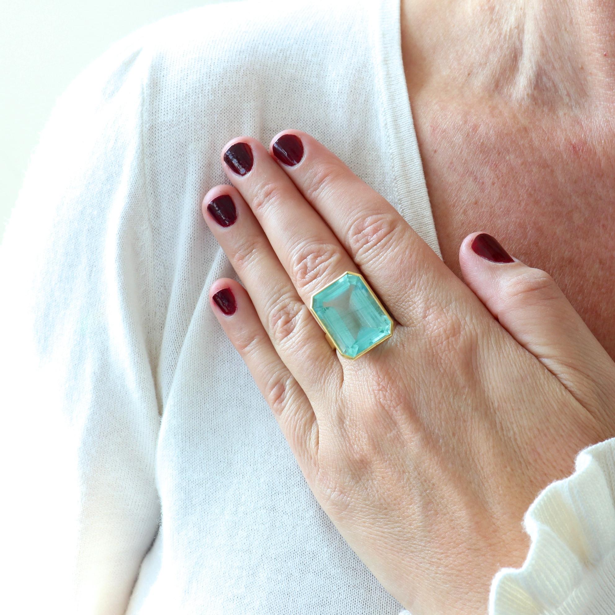 Sublime greenish blue, 23 carat emerald cut aquamarine is bezel set in 22k gold with 14k gold geometric cut outs, and 18k gold ring shank left open at top to illuminate the beautiful aquamarine. Ring size 7 1/2 and comes with complimentary sizing if