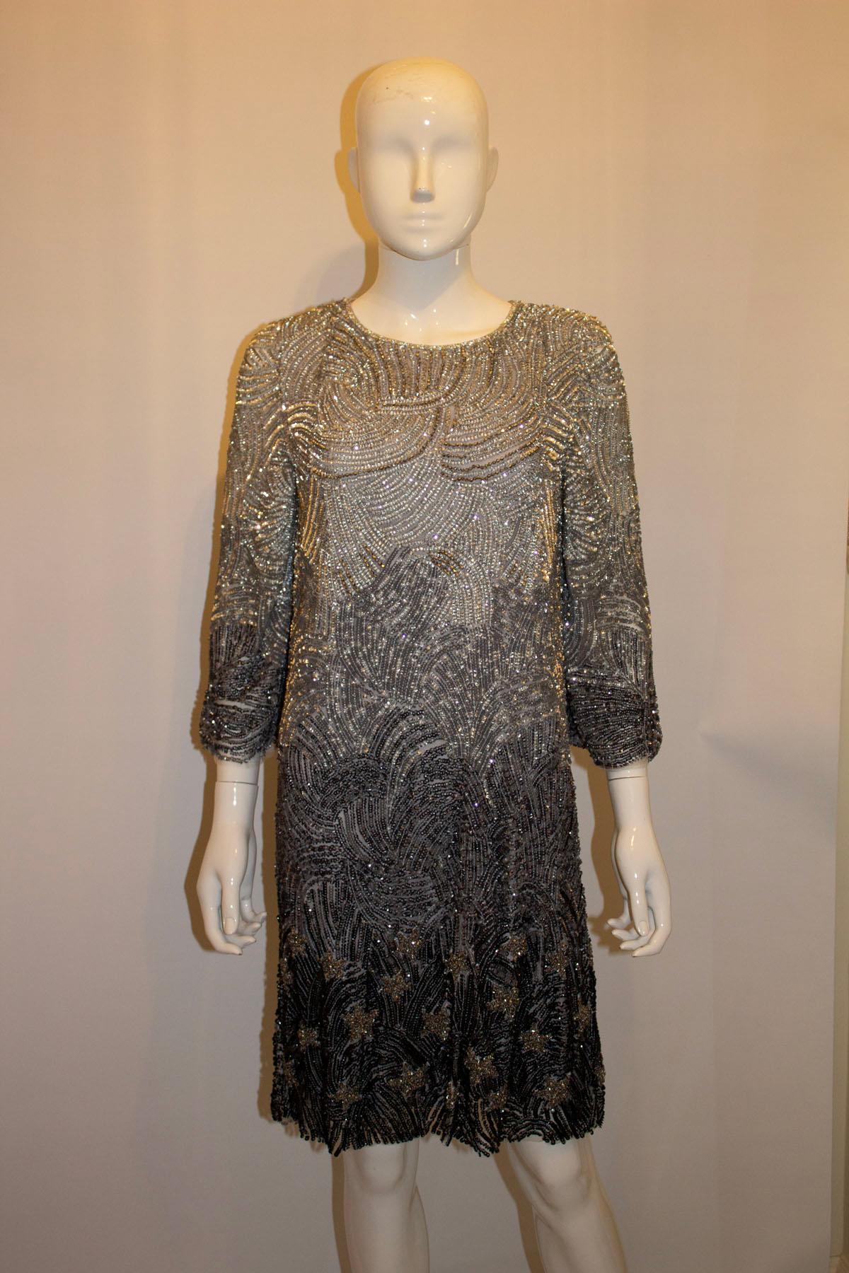 Ein superschickes und lustiges Cocktailkleid von Jenny Packham, Mainline. Das Kleid hat wunderbare Perlen Details in einem Stern-Design  in verschiedenen Grautönen. Es hat einen runden Ausschnitt, ellenbogenlange Ärmel  und ist vollständig 