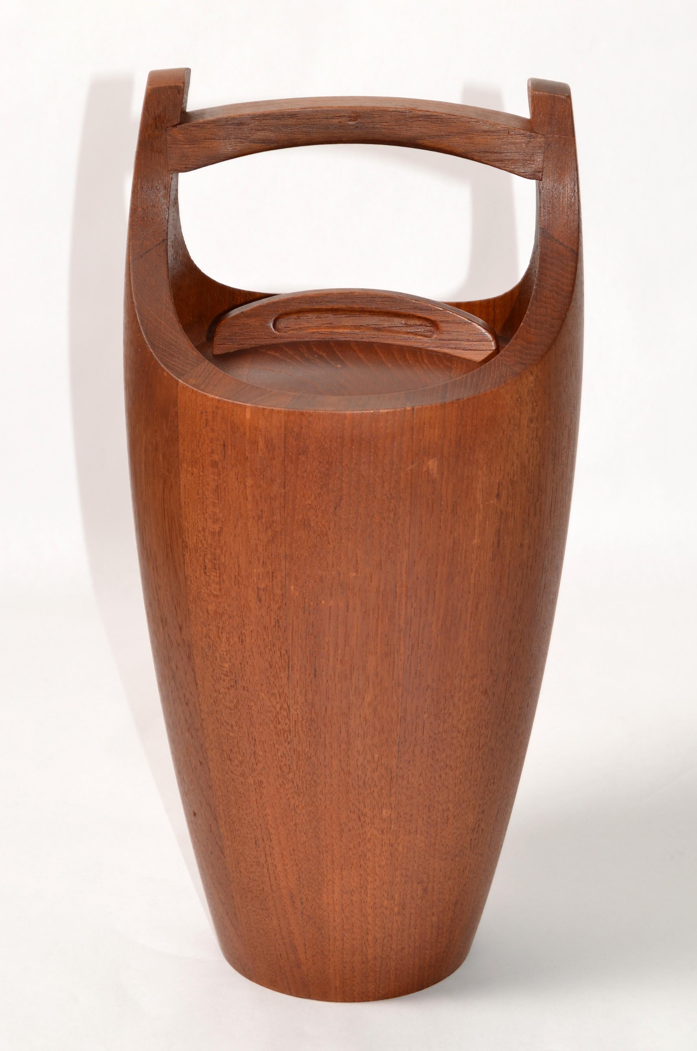 Cubitera moderna danesa con tapa, de madera de teca, diseñada por Jens Quistgaard para Dansk Designs.
El interior está forrado de plástico naranja y la tapa se asienta firmemente sobre él.
Marcada con la primitiva marca Dansk, sede central de