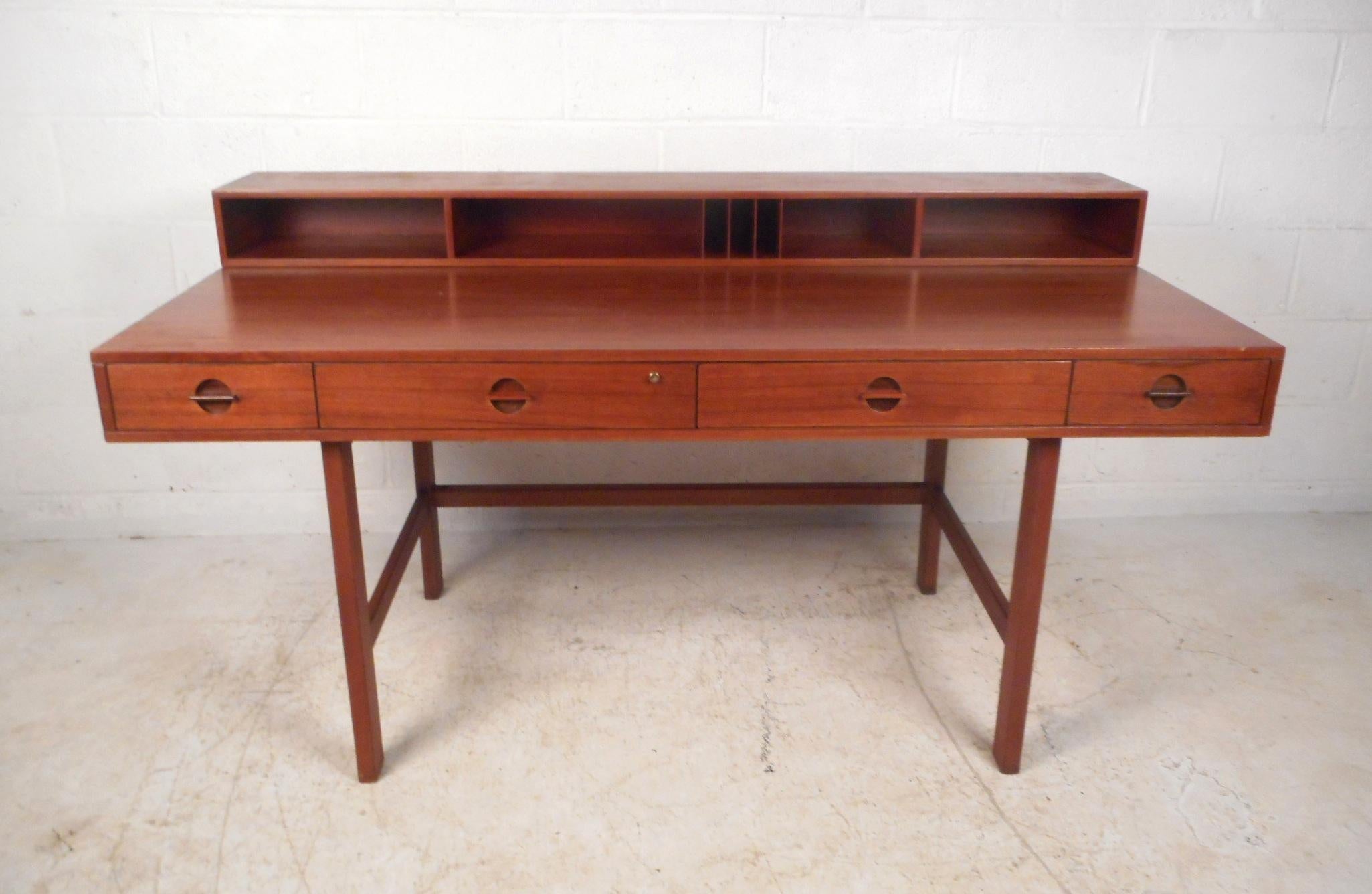 A versatile midcentury desk with plenty of room for storage and a flip top with storage trays and cubbies. This stunning Danish modern desk boasts a rich teak finish, four large drawers, and stretchers along the base for added sturdiness. When the