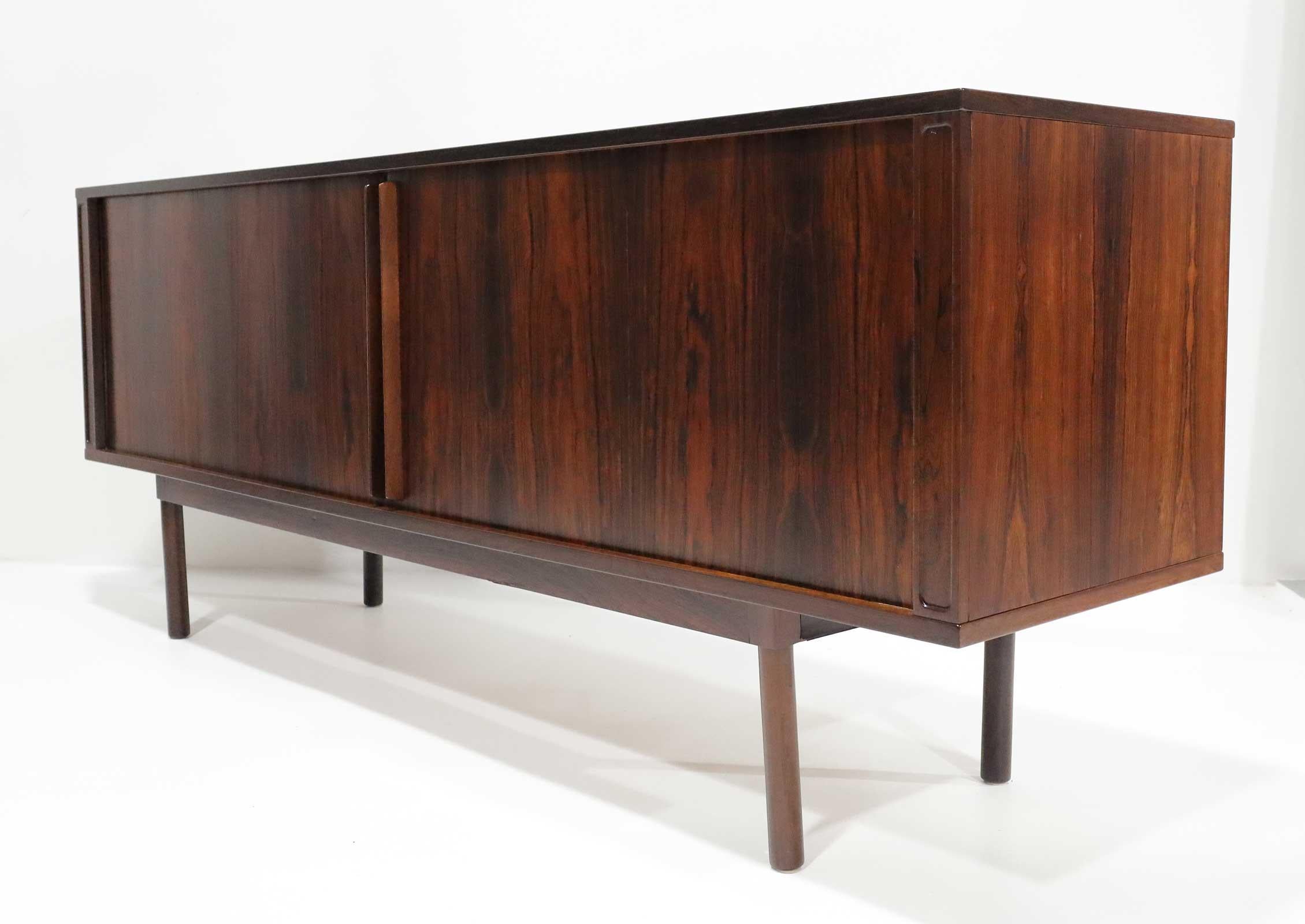 Splendida credenza in legno di palissandro di Jens Quistgaard per Peter Lovig con ante a tamburo, che si aprono su un banco centrale di cassetti, affiancato su entrambi i lati da ripiani, sollevati su gambe cilindriche. La schiena è