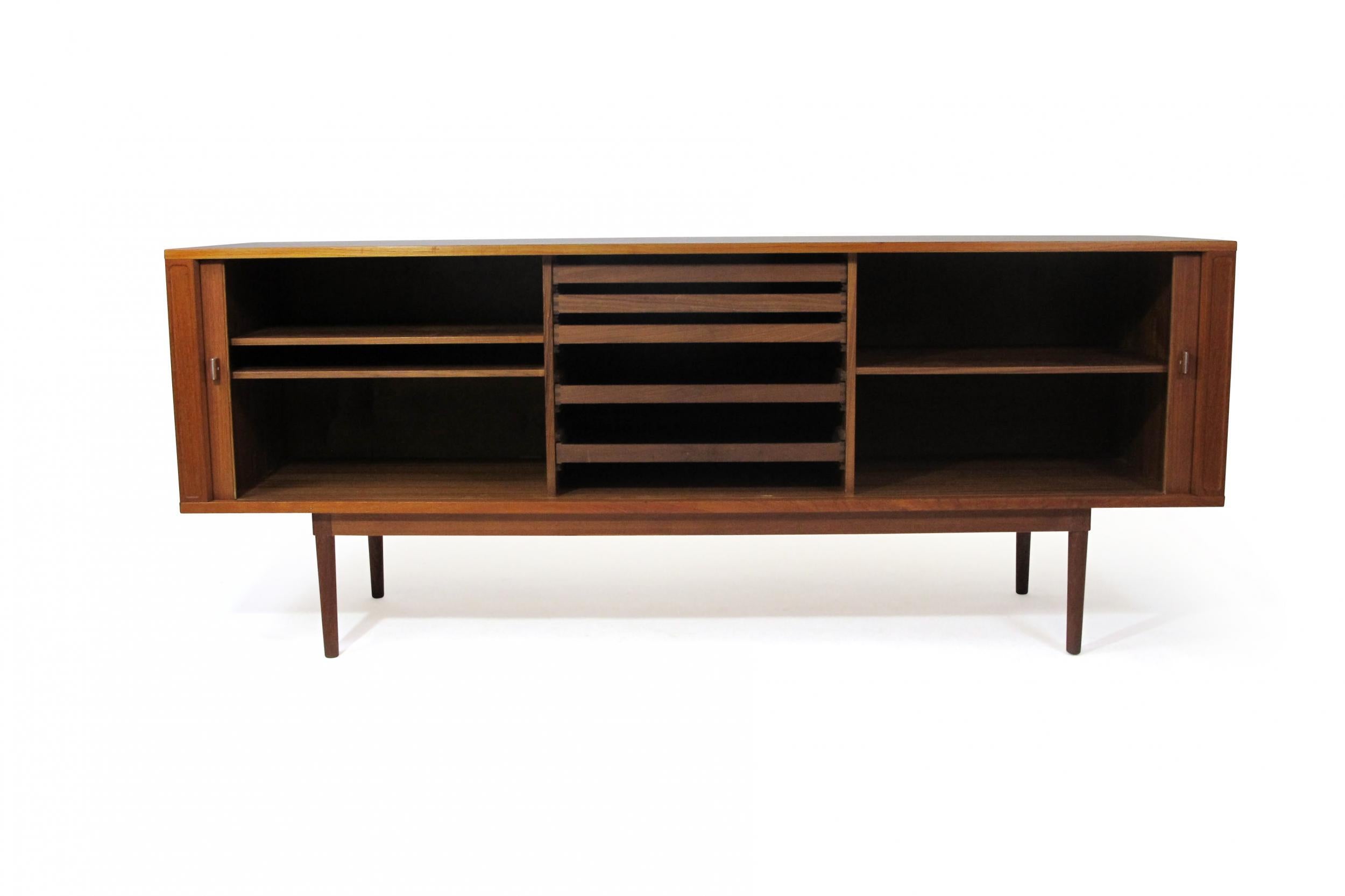 Teak credenza designed by Jens Quistgaard for Peter Lovig, Denmark, c.1960. The sideboard is crafted of teak with a book-matched tambour door front, which opens to reveal a series of adjustable shelves and silverware drawers. Raised on round tapered