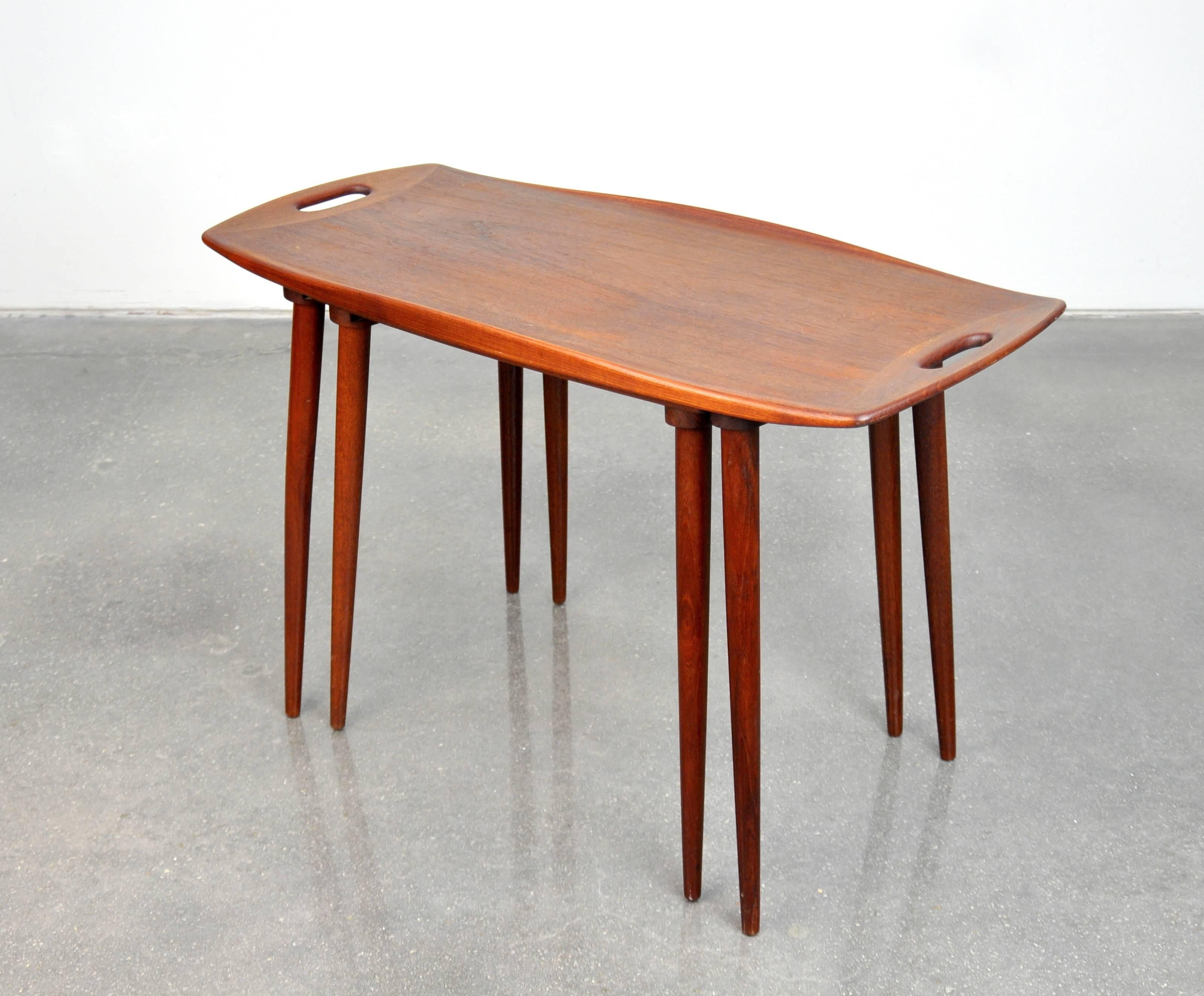 A pretty Danish modern teak tray table, with nesting smaller table, designed by Jens Quistgaard and made in Denmark by Nissen in the mid-1960s. The sculpted top features finger cut-outs at each end, raised edges and slender, tapered legs. A