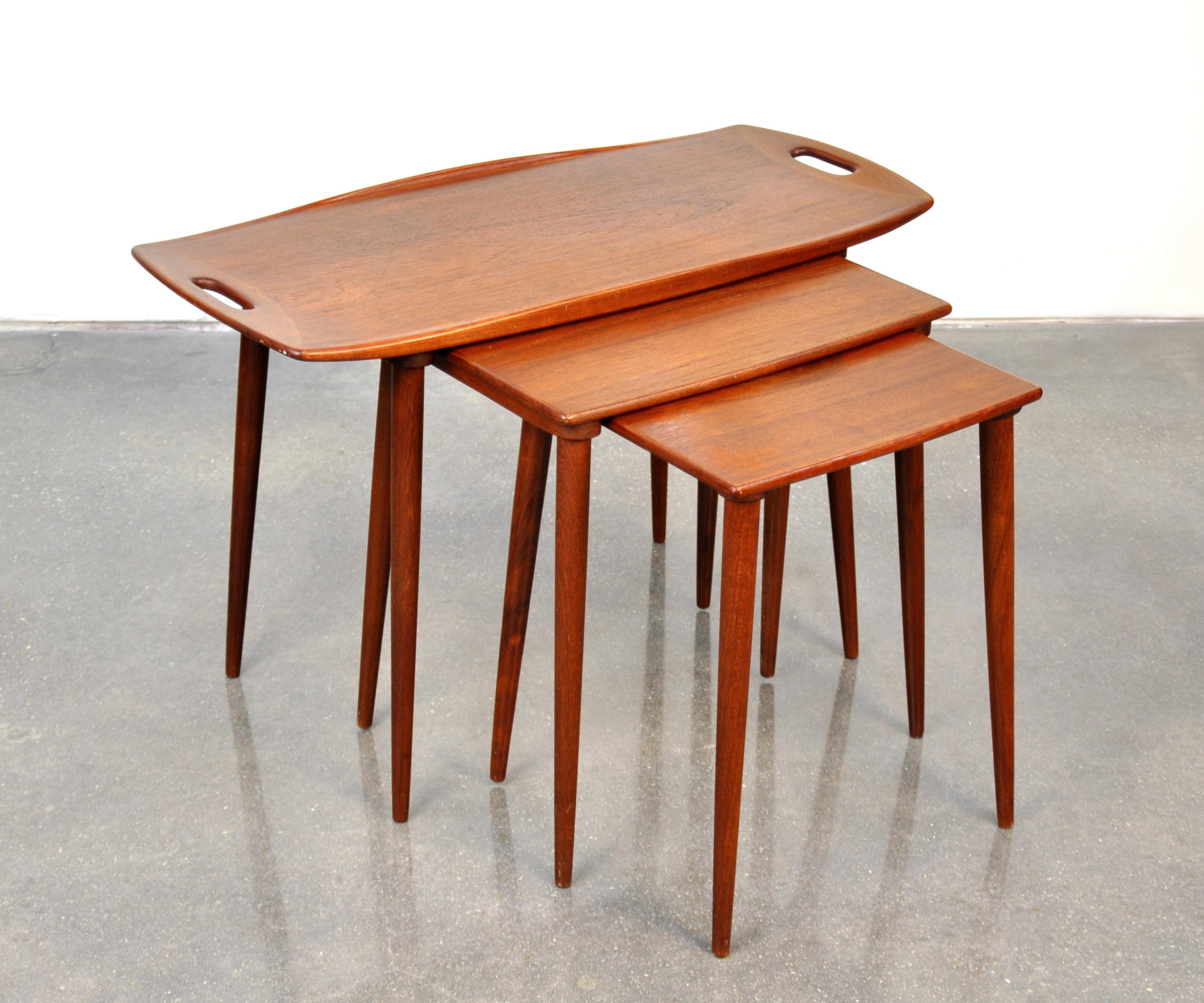 A vintage midcentury Danish modern teak tray table, with a pair of smaller nesting side or end tables, designed by Jens Quistgaard for Richard Nissen. The sculpted top of the largest table features finger cut-outs at each end, raised edges and