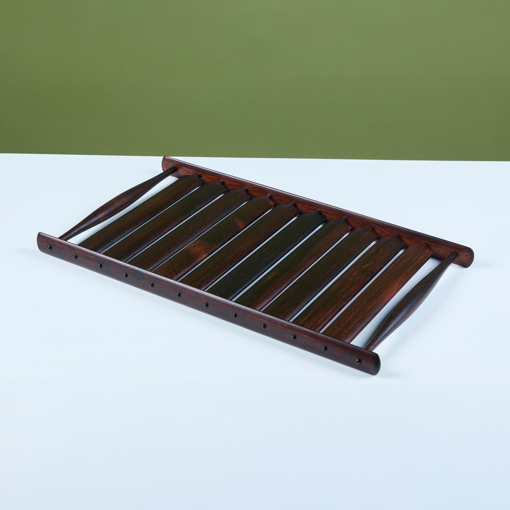 Bandeja diseñada por Jens H. Quistgaard para la colección Dansks Rare Woods, c.1960, Dinamarca. Presenta madera de palisandro esculpida con asas de espiga y listones de madera a lo largo de la bandeja.

Dansk es uno de los fabricantes más queridos y