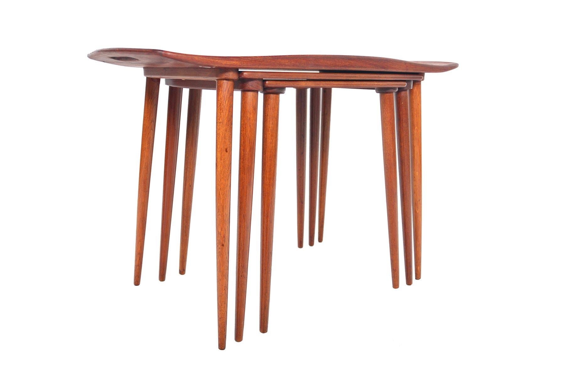 This rare set of Jens Quistgaard nesting tables is crafted in teak. Exterior table offers raised sides with carved handles. All tables stand on teak spindle legs. In excellent condition.