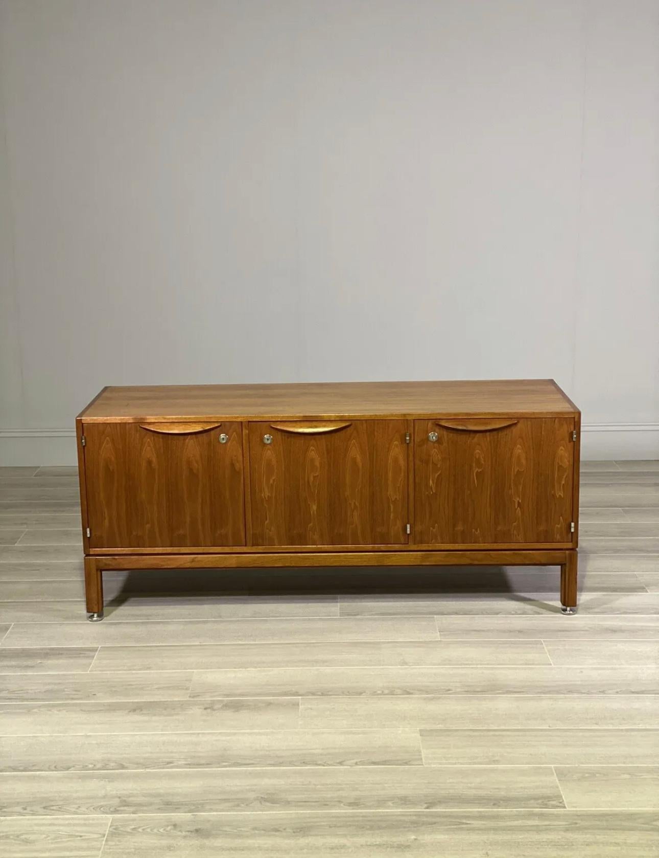 A mid century credenza made by the American Danish designer Jens Risom. A stylish piece that sits on adjustable chrome feet with American black walnut envelope veneers throughout. A quality piece in good overall condition with slight scratches to