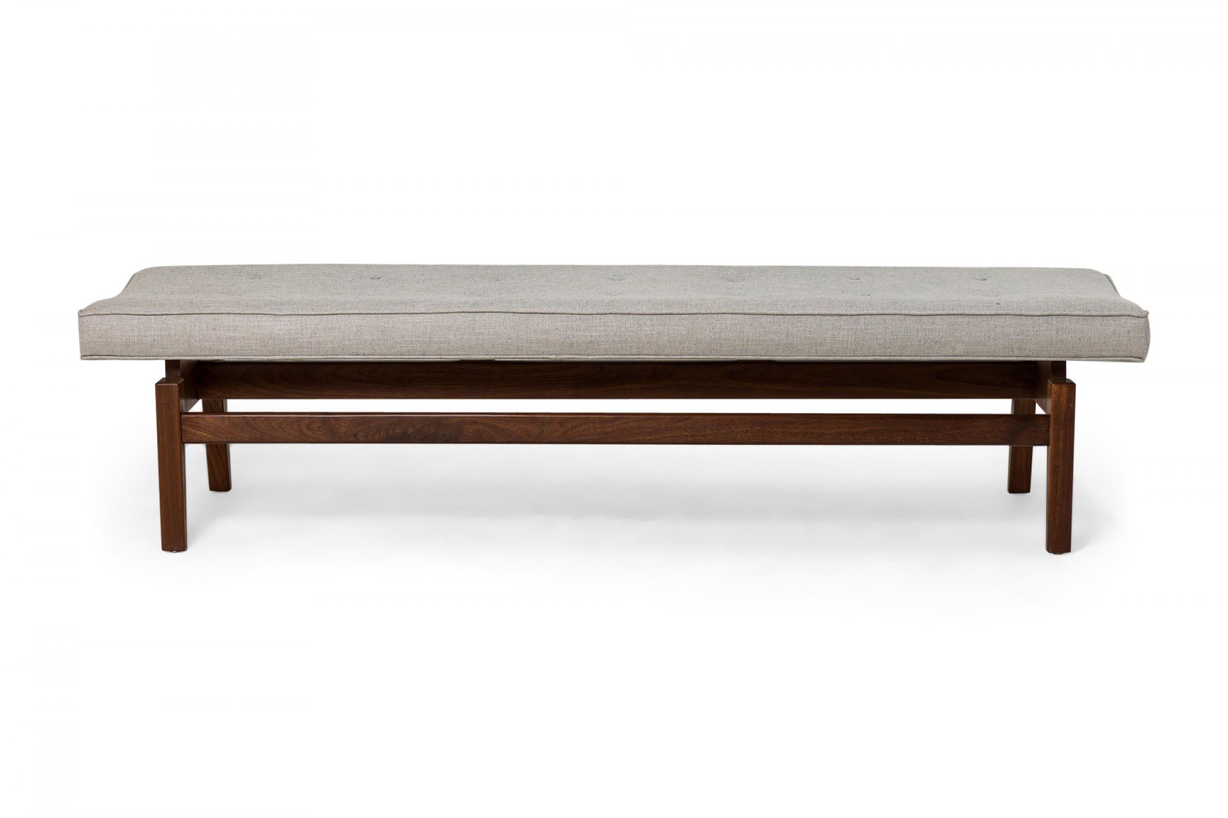 Danish Mid-Century floating bench with a walnut stretcher base supporting a rectangular seat cushion upholstered in light gray woven fabric with button tufted detail. (JENS RISOM).
 
