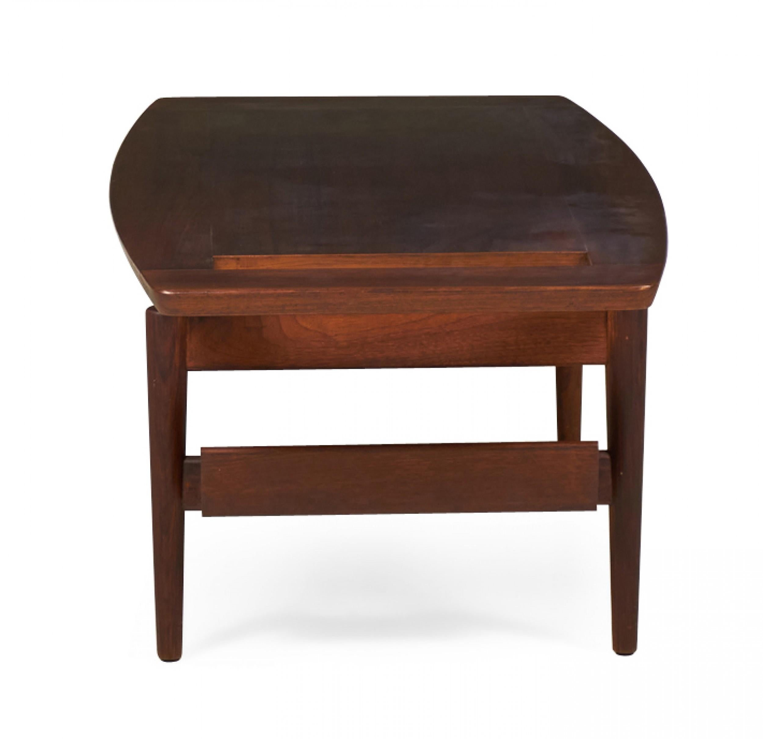 Danish Mid-Century walnut coffee table with a rectangular top with tapered edges and a rectangular cutout on one side resting on a stretcher base with built-in magazine rack and four tapered legs. (JENS RISOM) (Similar table: DUF0098A)
