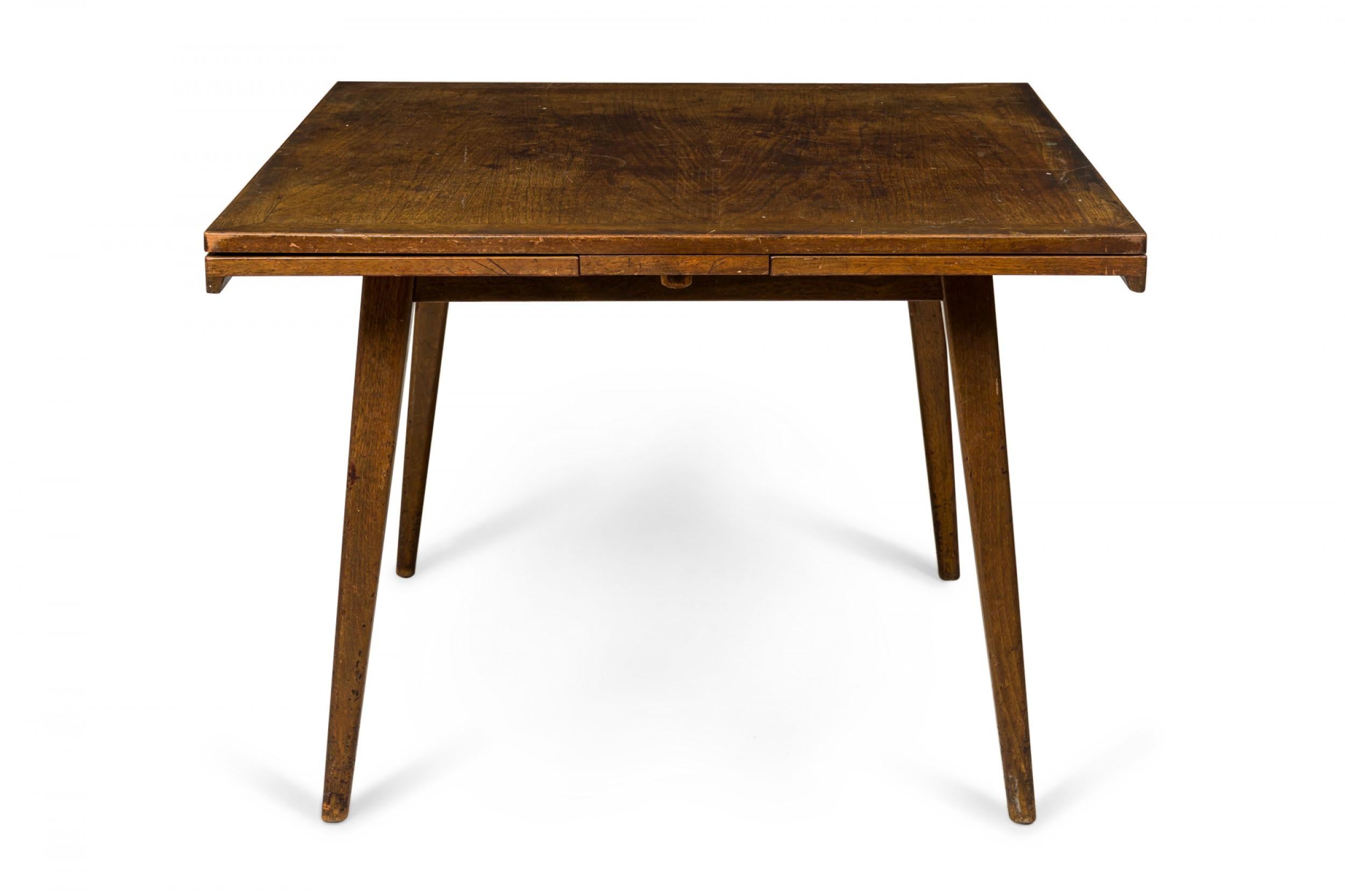 Danish Mid-Century walnut draw leaf dining table with a square top that pulls open from two sides to expand the table top surface, resting on four tapered dowel legs. (JENS RISOM)
