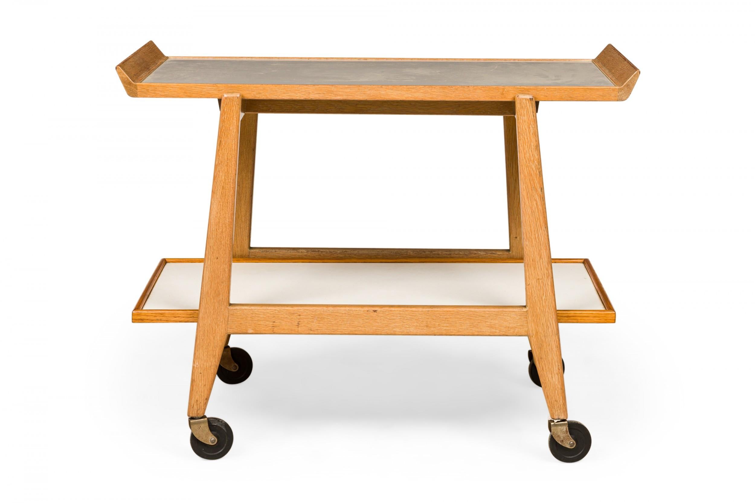 Danish Mid-Century two-tier serving trolley with an oak frame, light gray laminate shelf surfaces, and a removable tray top, resting on four casters. (JENS RISOM)
