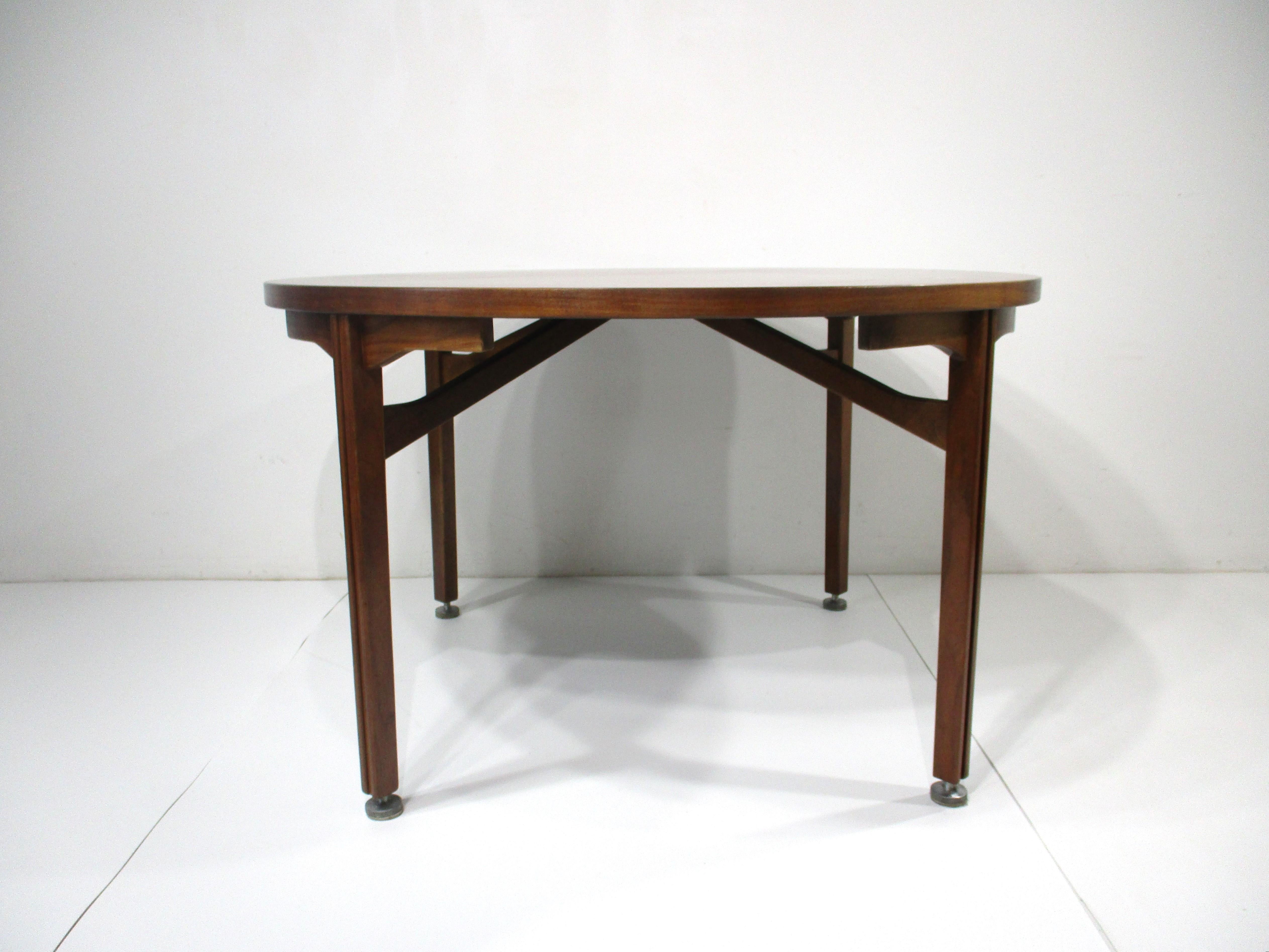 A very well crafted medium dark walnut round dining table with sturdy legs having a groove line in each one and cast aluminum foot pads . Designed by Jens Risom for his company Jens Risom Designs , the top has wonderful graining giving the piece a