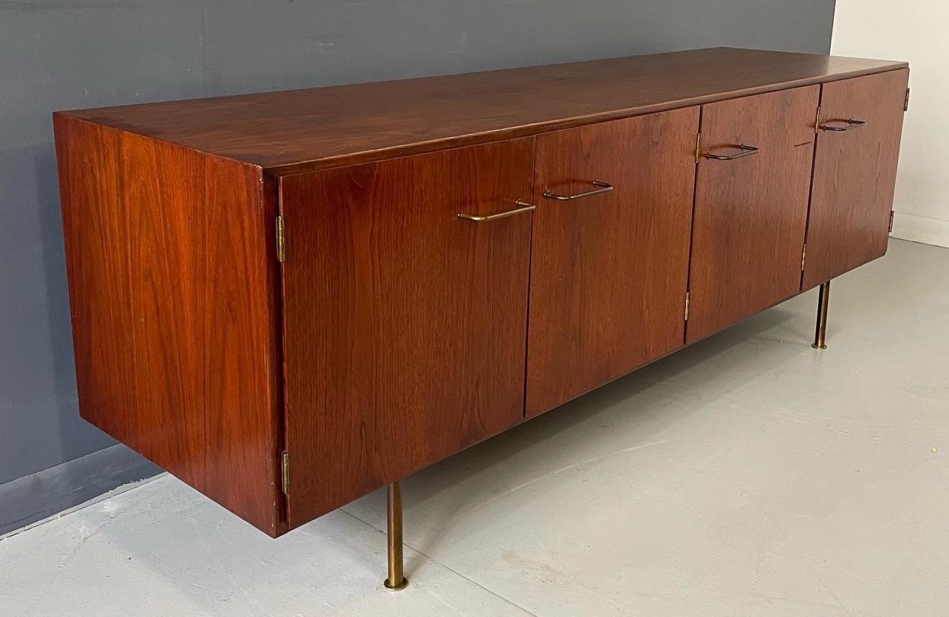 This is an early Jens Risom solid walnut credenza that has four doors each revealing a space with one shelf. Brass pulls and brass cylinder legs make this credenza special.