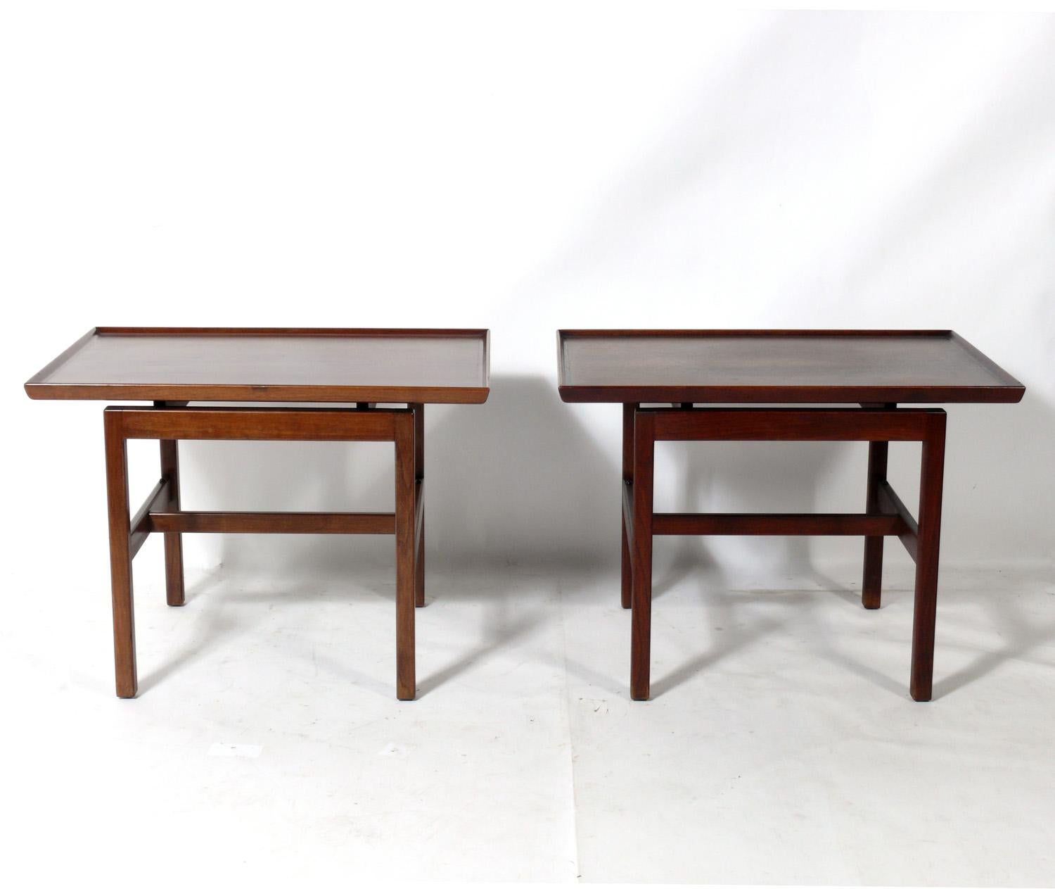 Pair of clean lined mid century walnut side tables or night stands, designed by Jens Risom, circa 1960s. They are being refinished and will look amazing when completed. The price noted includes refinishing. They have glass shelves at the bottom.