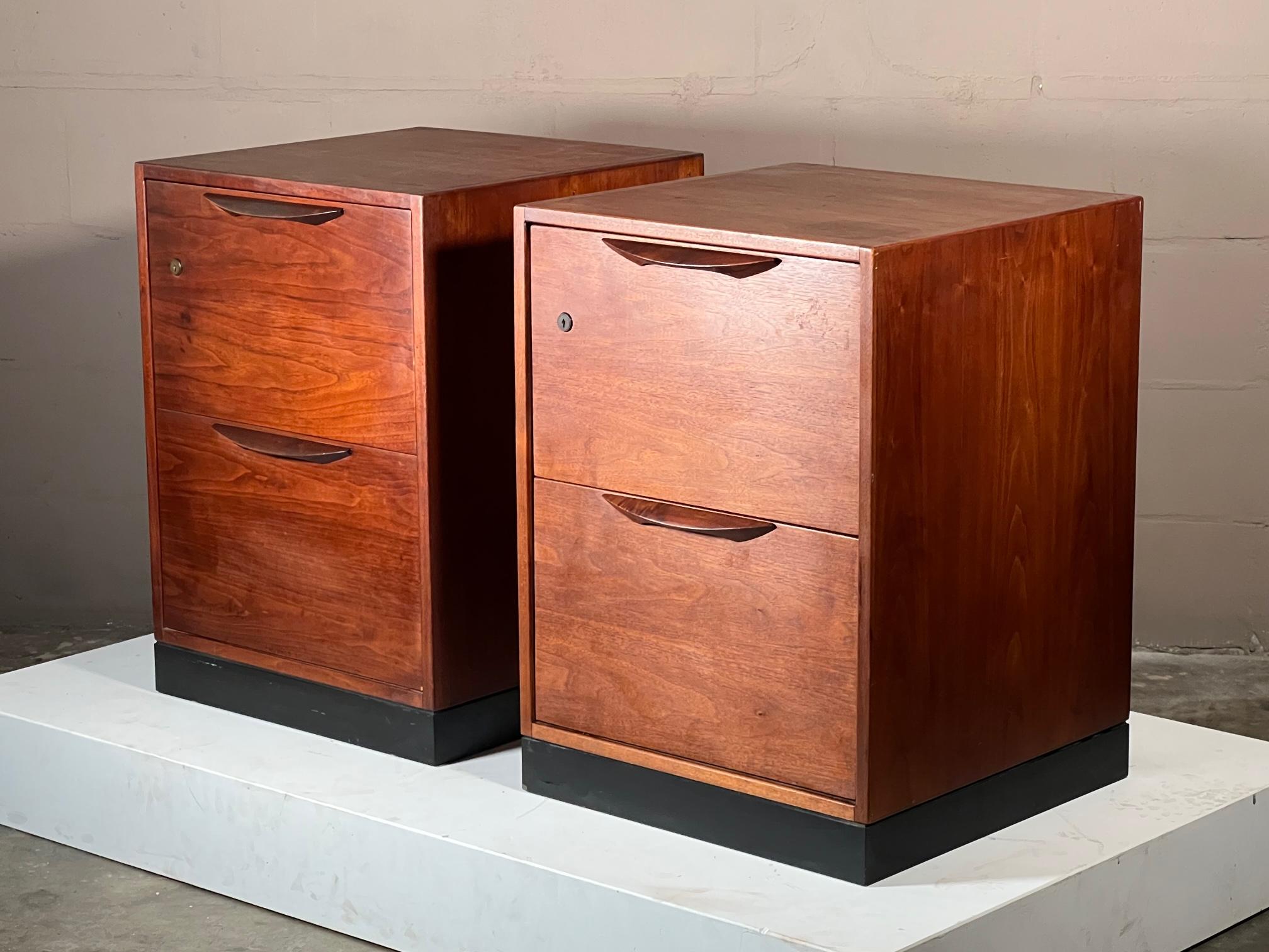 A pair of classic filing cabinets by Jens Risom, ca' 1960's. Made of walnut with sculpted handles and finished backs. These versatile, cube shaped cabinets could be used as night stands, pedestals for a desk, etc.