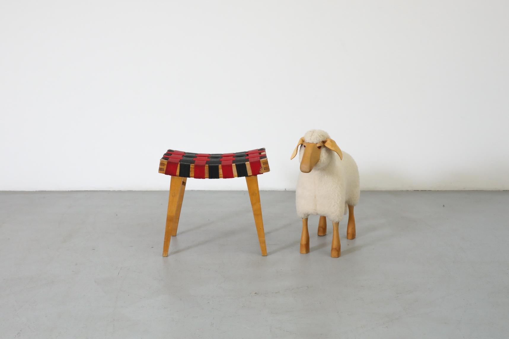 Petit tabouret de style Jens Risom avec sangles rouges et noires d'origine. Le cadre de l'assise est légèrement incurvé, avec une belle construction à queue d'aronde et à chevilles, et les pieds sont effilés. En état d'origine avec une usure