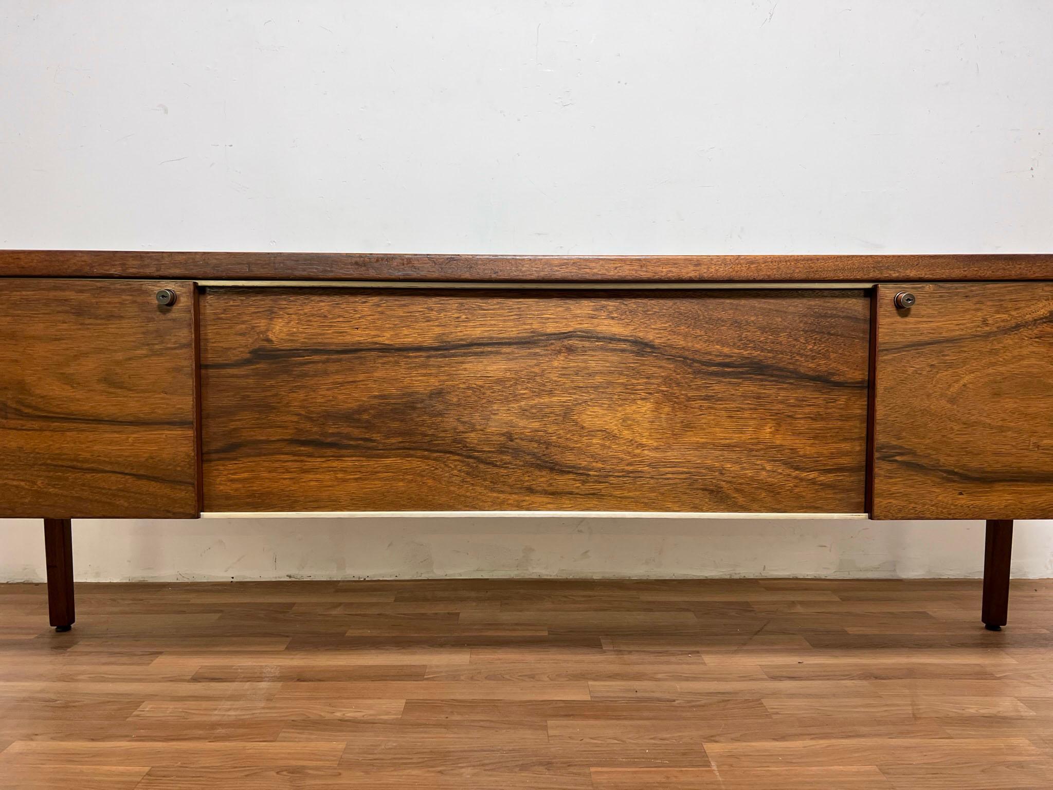 An executive credenza in highly figured walnut -- resembling rosewood -- by Jens Risom, ca. 1960s. Features shallow drawers on the left, storage on the right, and two sunken file drawers at top center. Note, the pentaflex file holders and the center