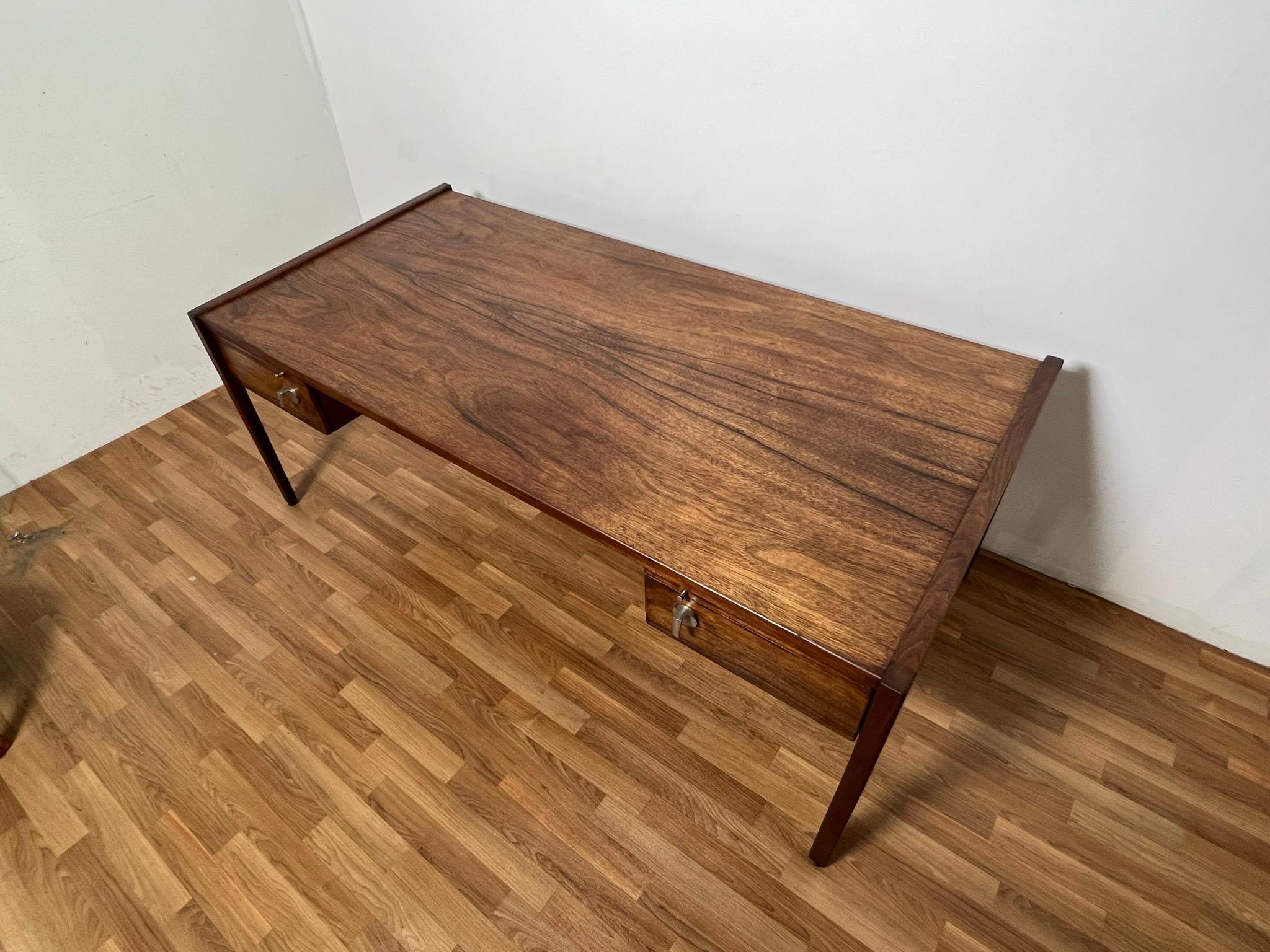 An executive desk in highly figured walnut -- resembling rosewood-- with two shallow flanking drawers, and two draw-out writing returns by Jens Risom, ca. 1960s. Desk top height slightly tapers from back to front (like a subtle drafting desk),