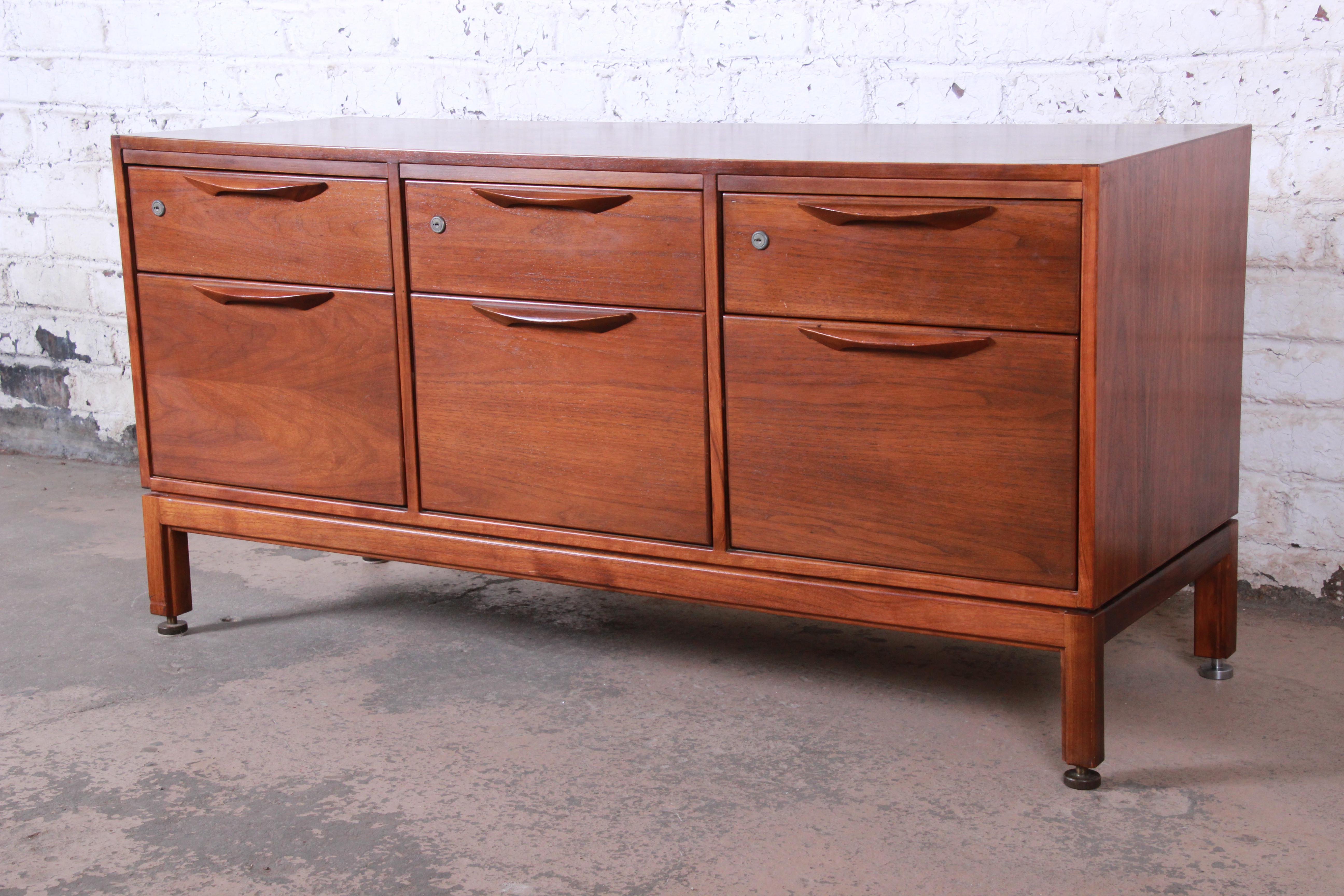 An exceptional Mid-Century Modern walnut credenza designed by Jens Risom. The credenza features stunning walnut wood grain and sleek midcentury Danish-inspired design. It offers ample storage, with six dovetailed drawers each with solid sculpted