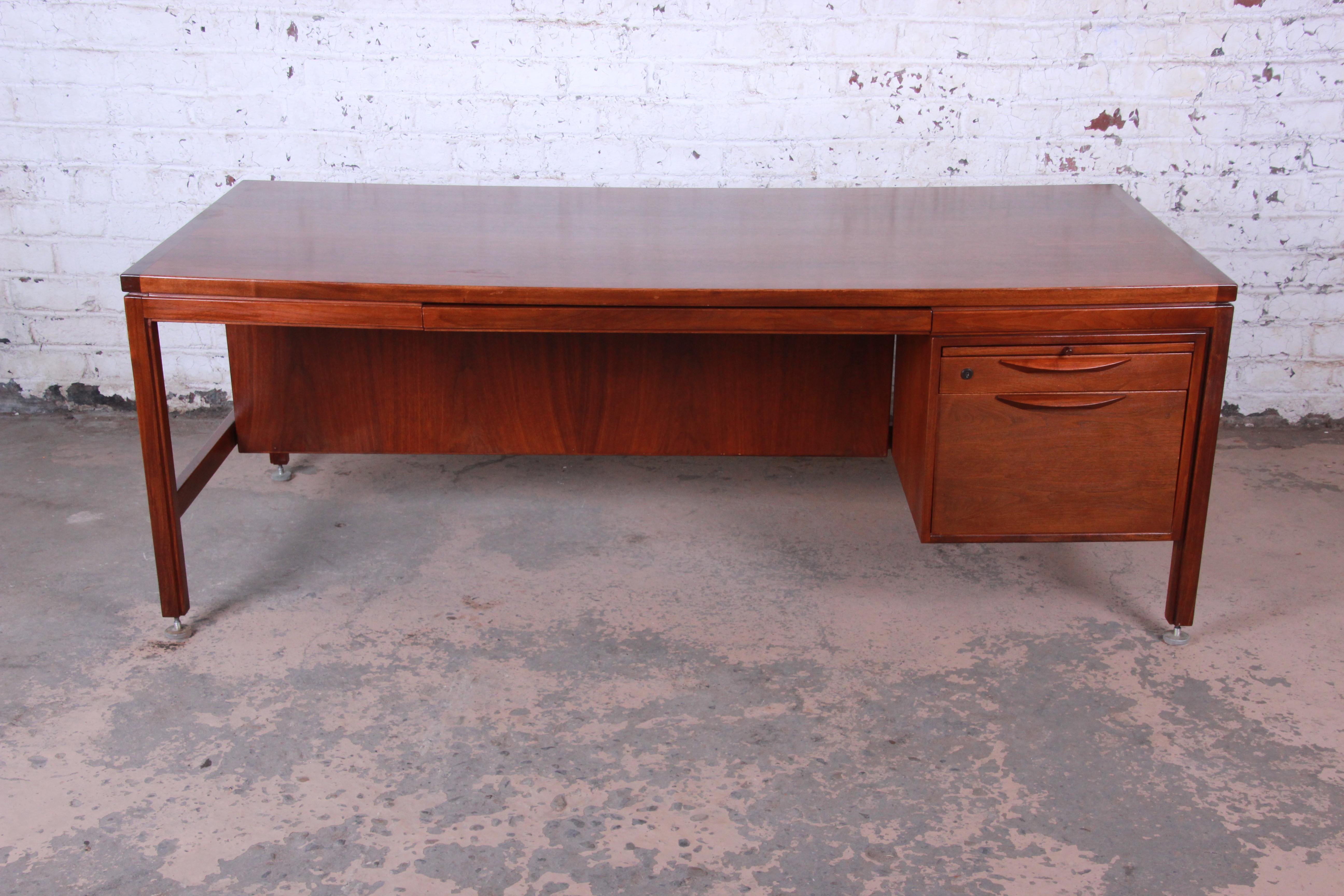 An exceptional Mid-Century Modern walnut executive desk designed by Jens Risom. The desk features gorgeous walnut wood grain and sleek Minimalist design. It offers good storage with two drawers, a pencil drawer, and a pull-out surface. Height can be