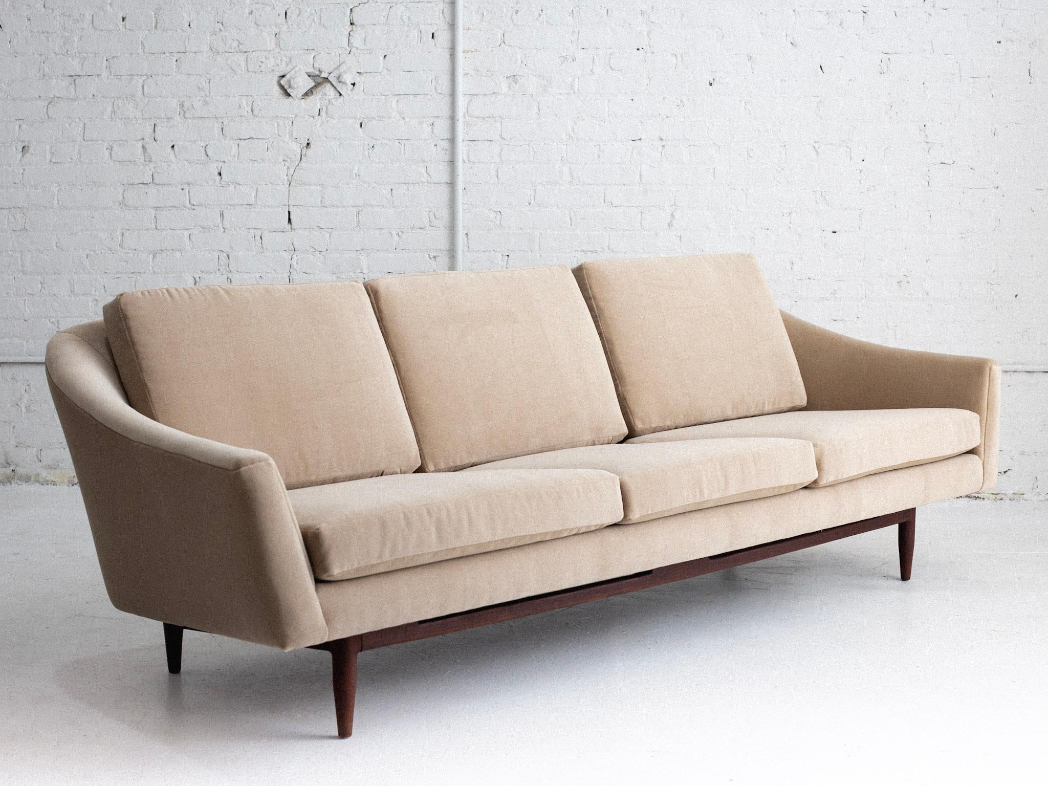 A mid century sofa attributed to Jens Risom. Sleek silhouette with curved arms and a walnut base. Newly reupholstered in a light beige velvet. 