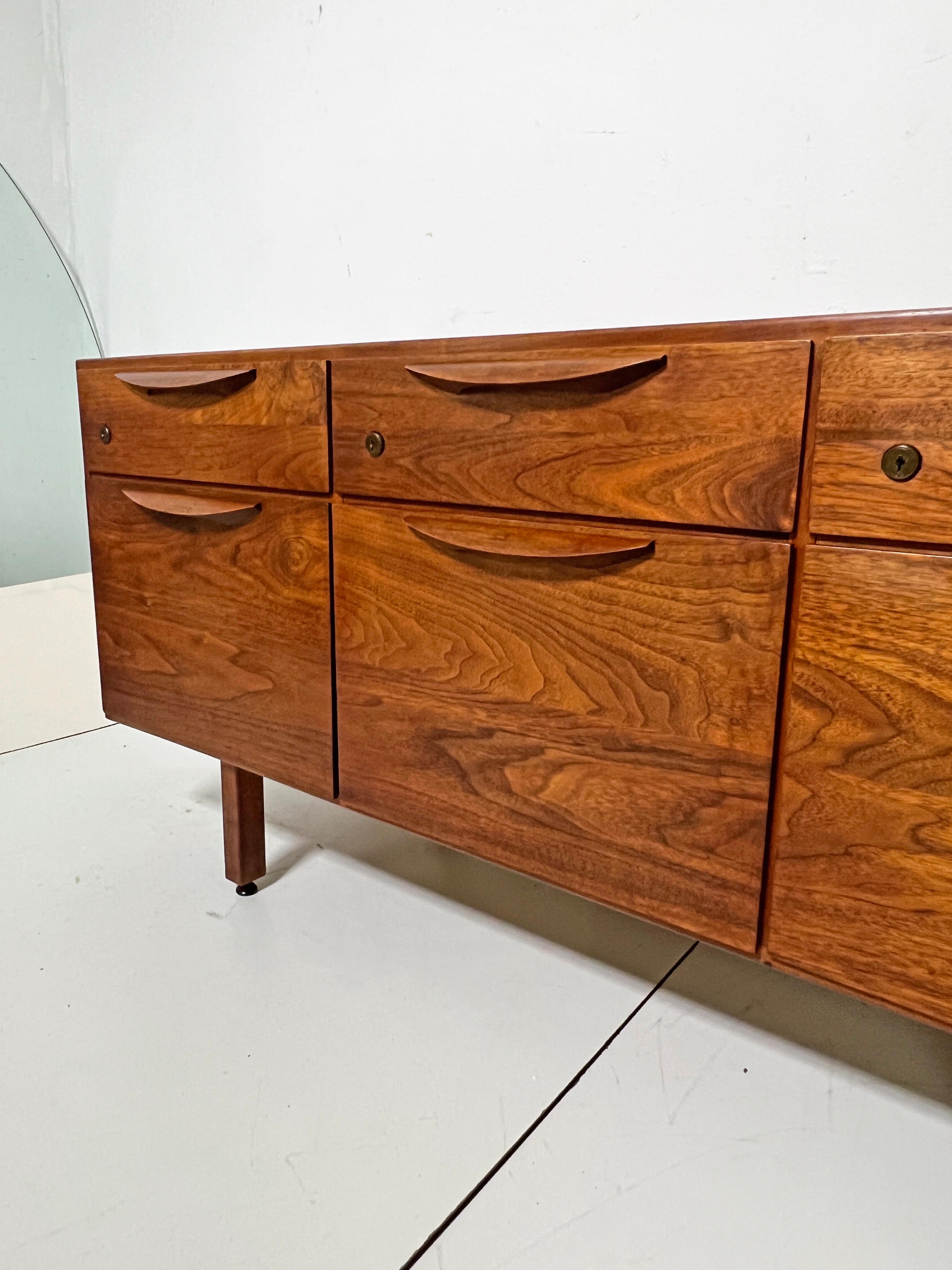 Mueble multimedia, aparador o cómoda de nogal de mediados de siglo, obra del diseñador danés-estadounidense Jens Risom, hacia la década de 1960. Los tres cajones superiores contienen cada uno un separador extraíble. Los tres cajones profundos