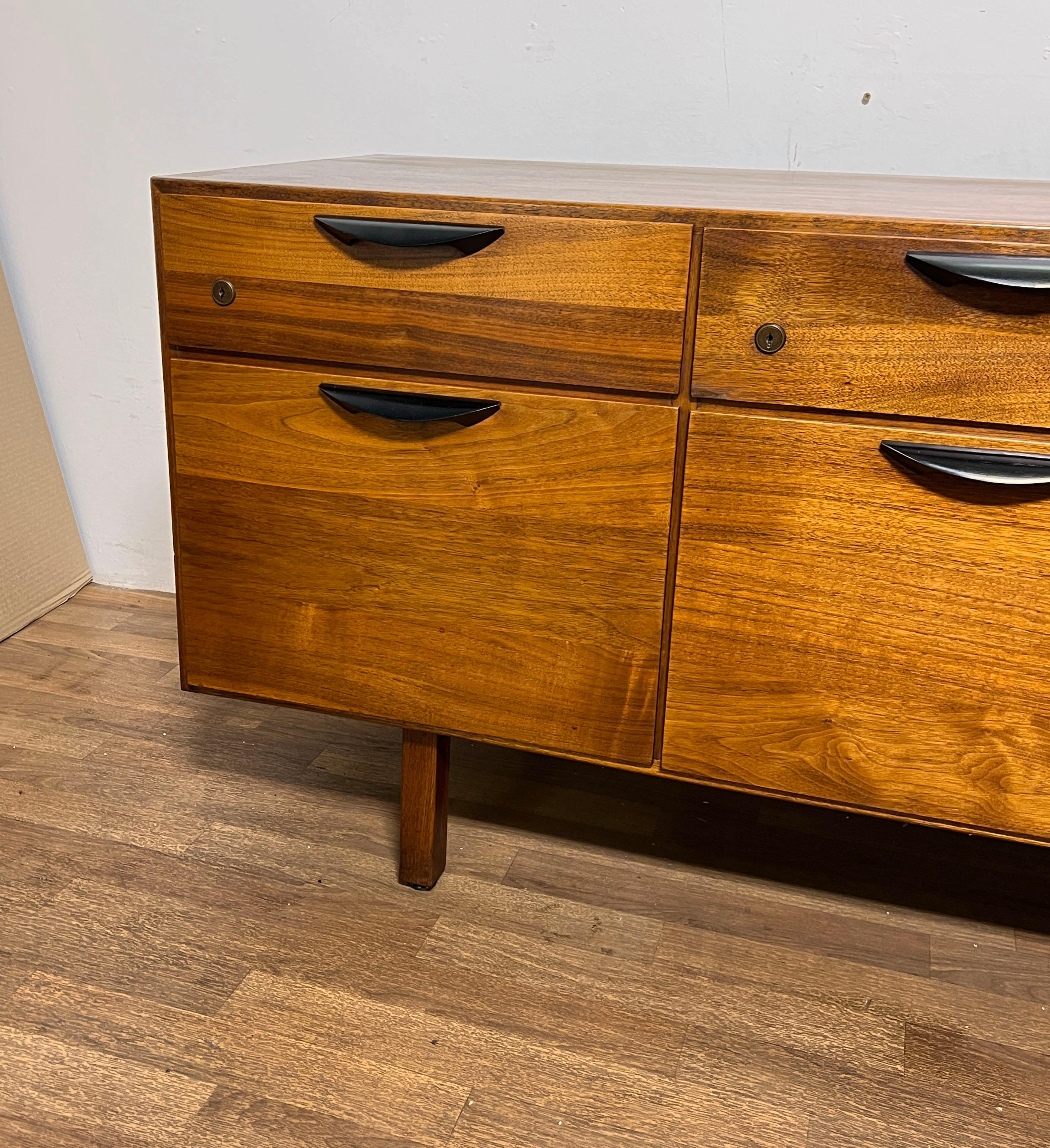 A credenza in walnut by Jens Risom, circa 1960s. Features filing cabinet drawers along the bottom and a compartment with a singular shelf on the left.  