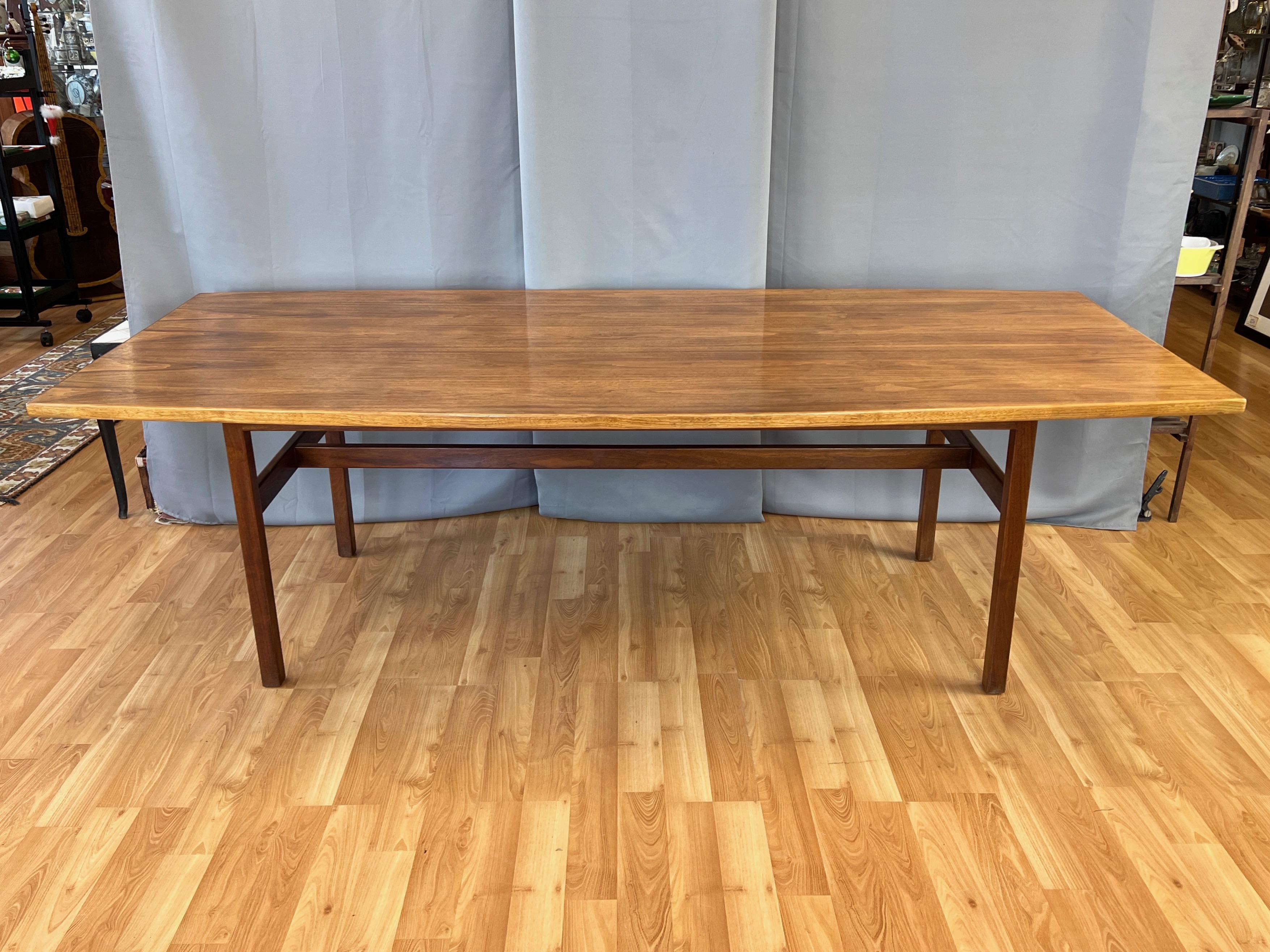 A 1960s mid-century modern eight-foot-long bowed-edge walnut dining table by Danish-American designer Jens Risom, a pioneer in introducing Scandinavian design principles to the United States.

Seats eight to ten, with the boat-shaped or