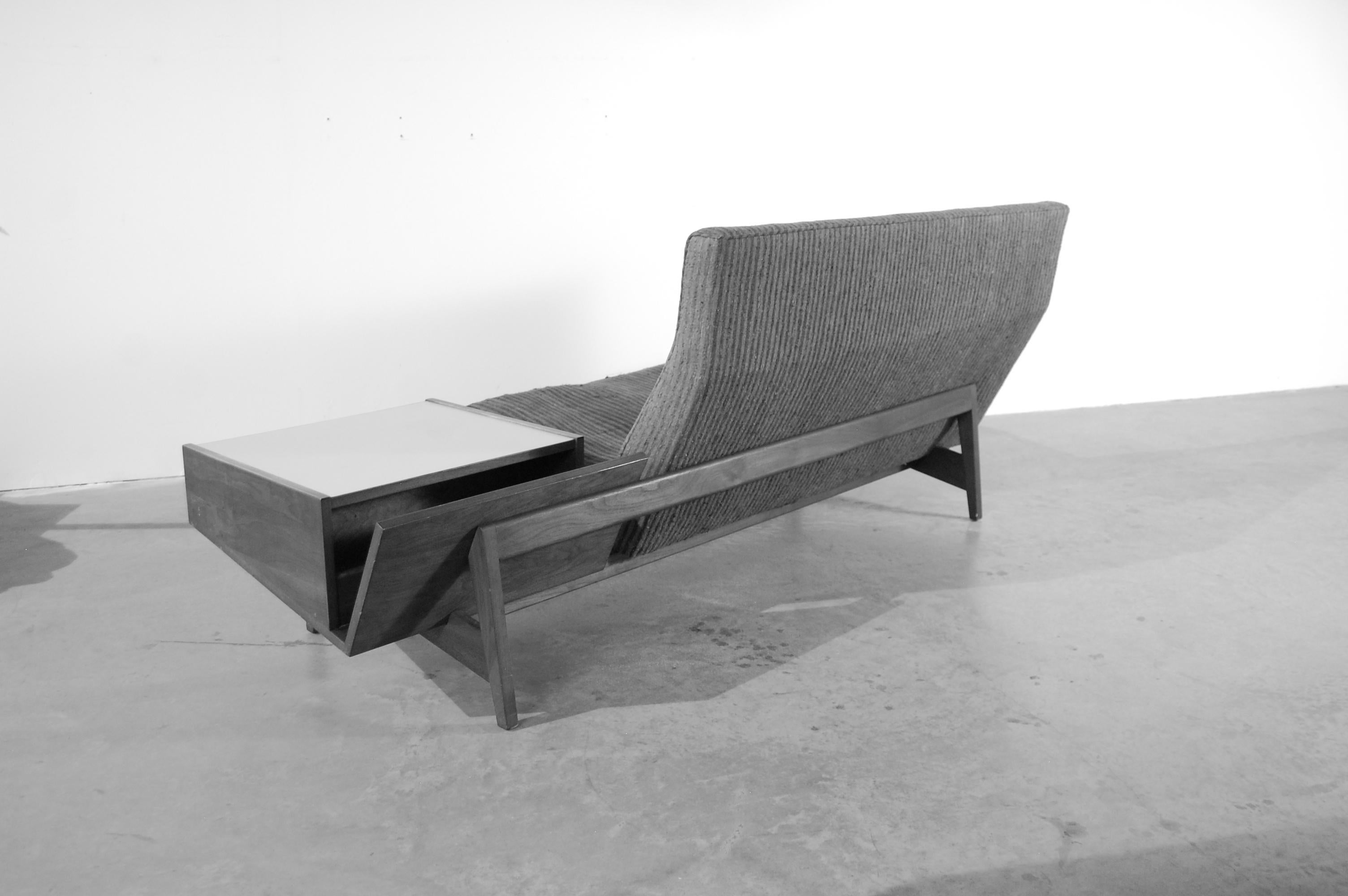 Jens Risom sofa, circa 1955, floating on a walnut frame, with a built in cantilevered storage table with magazine rack and cubbyhole to rear, and storage compartment to front. Please note: This sofa is being offered in 
