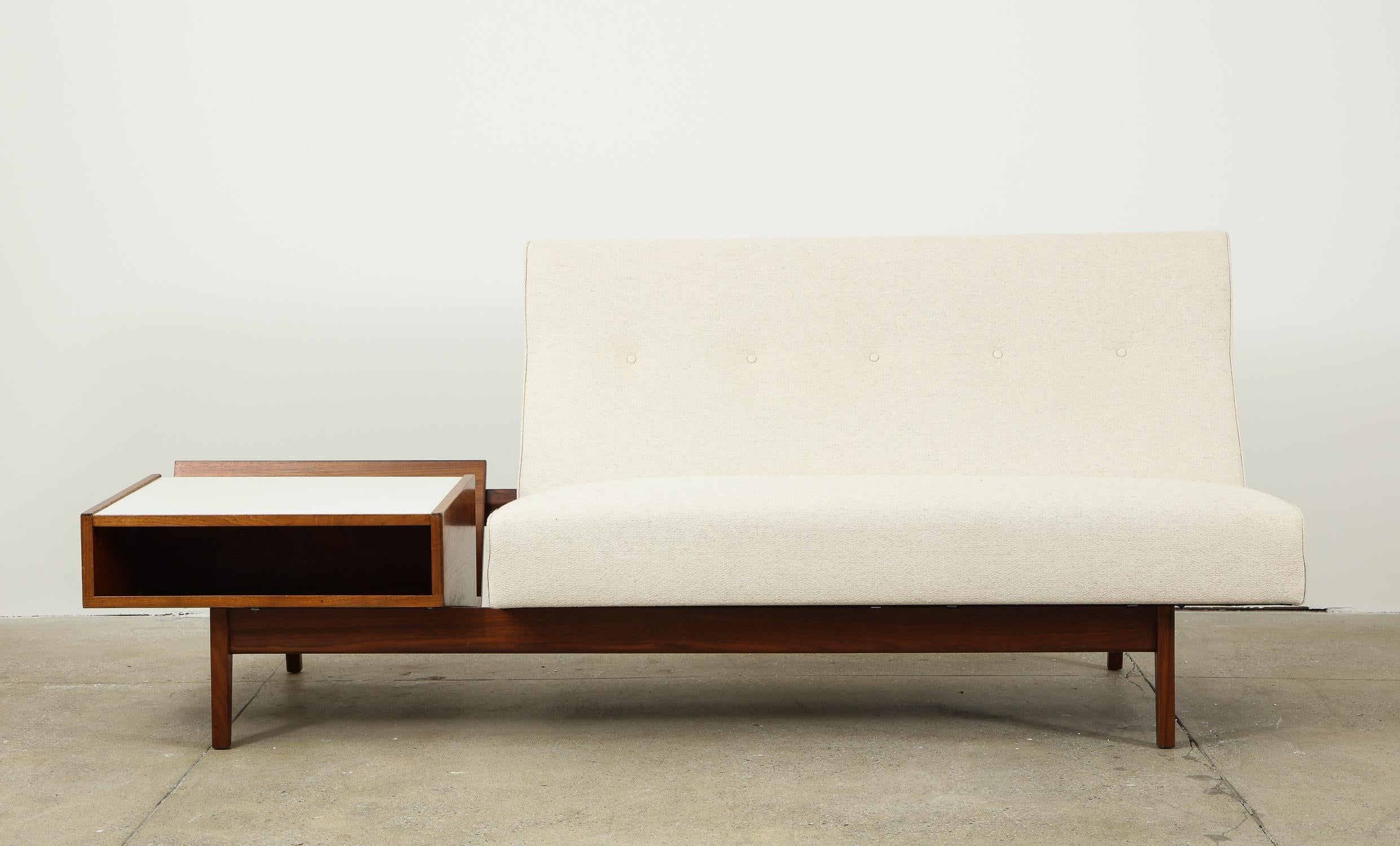 Jens Risom two-seat armless sofa with attached magazine table produced, circa 1958. The frame is walnut; the magazine table has its original white micarta top. A sleekly handsome and uncommon Risom design, shown in his eponymous catalog (Jens Risom