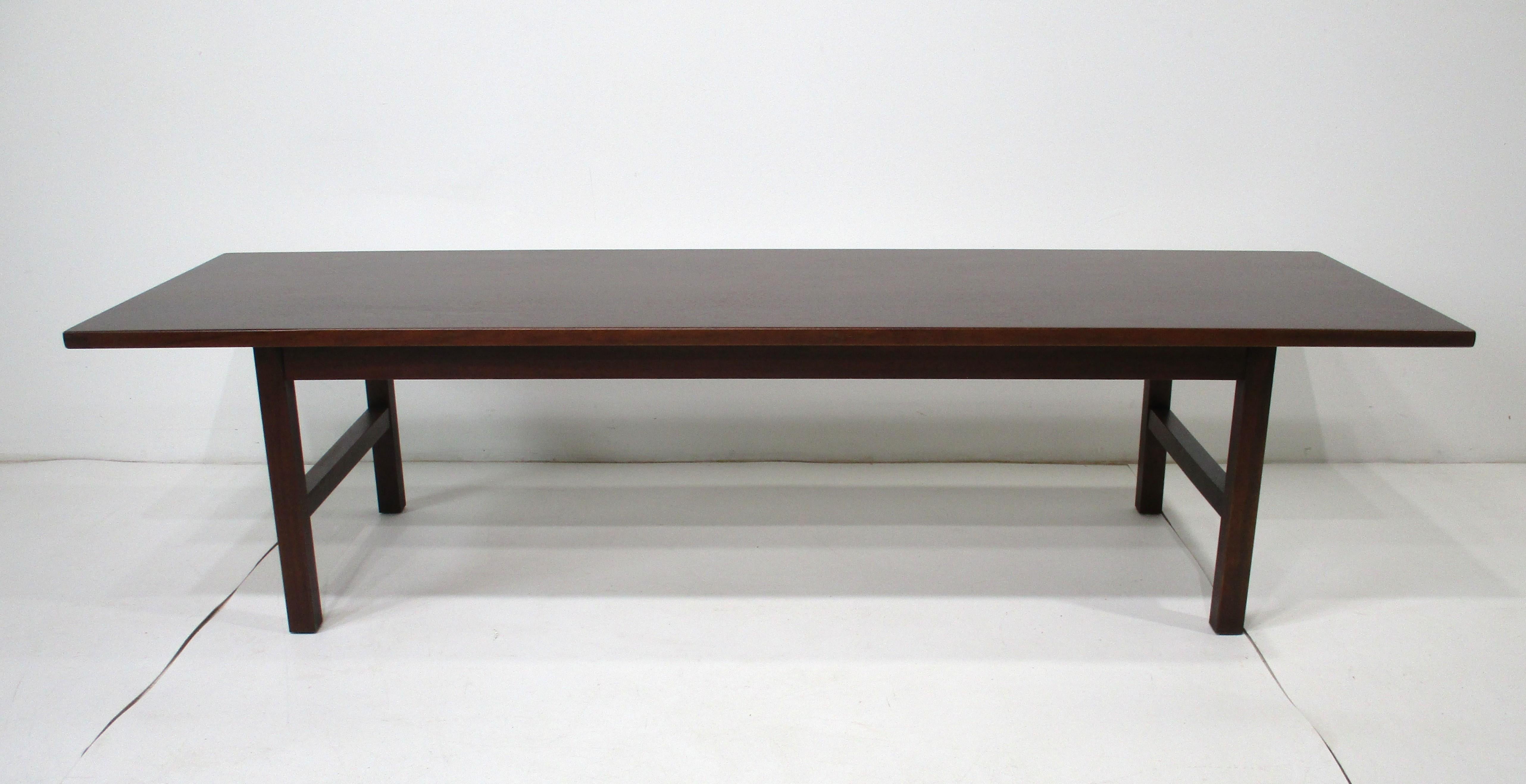 Table de cocktail en noyer foncé avec plateau rectangulaire reposant sur une base architecturale aux pieds caissonnés. Fabriquée à la manière du designer danois Jens Risom, cette pièce présente une esthétique fonctionnelle et épurée qui lui permet