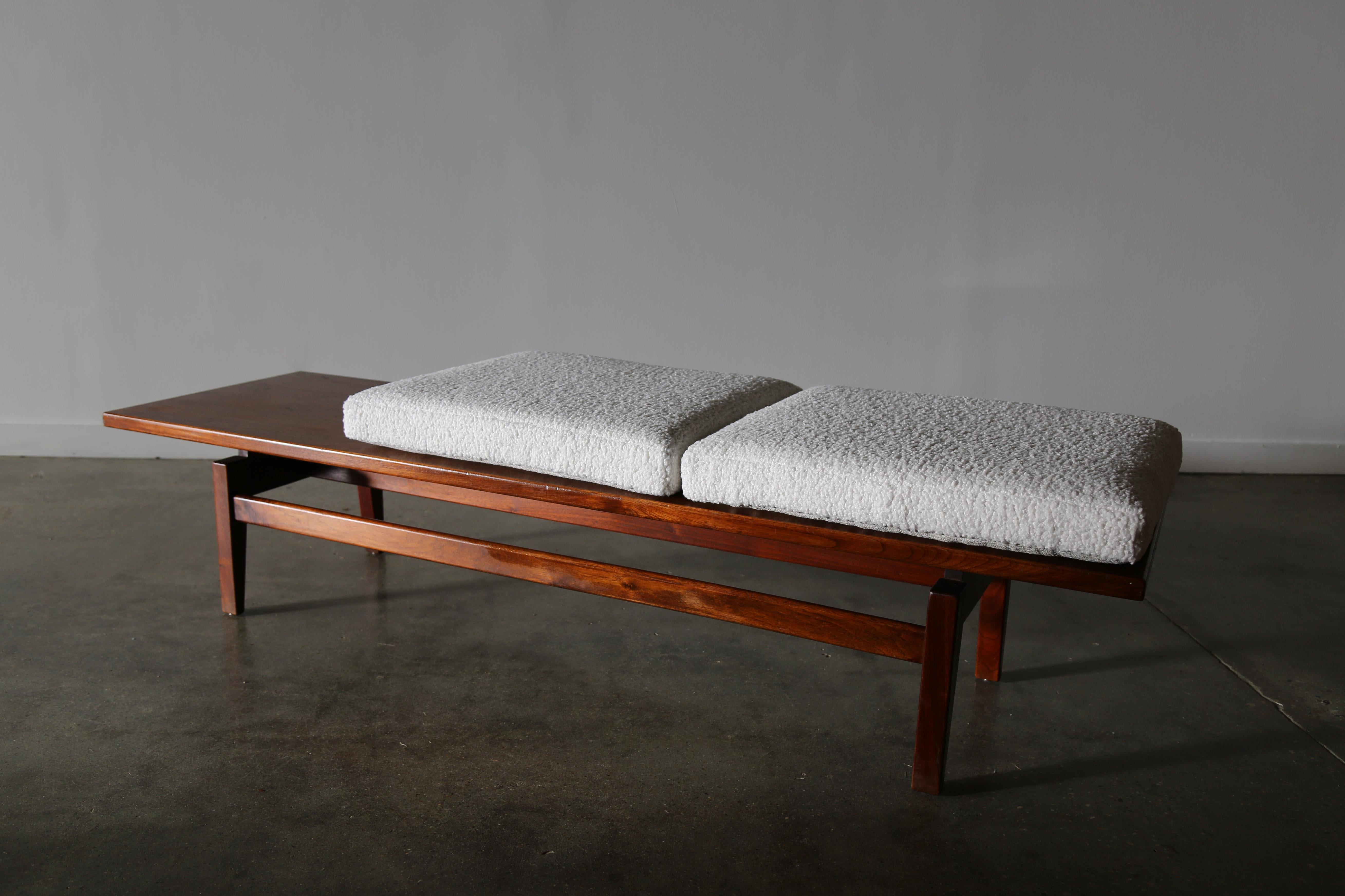 A bench / coffee table in walnut designed by Jens Risom circa 1950s. Expressive grain in the walnut veneer top suspended over solid walnut legs, which give the appearance of a floating top. White boucle cushions add a warm touch and stark contrast