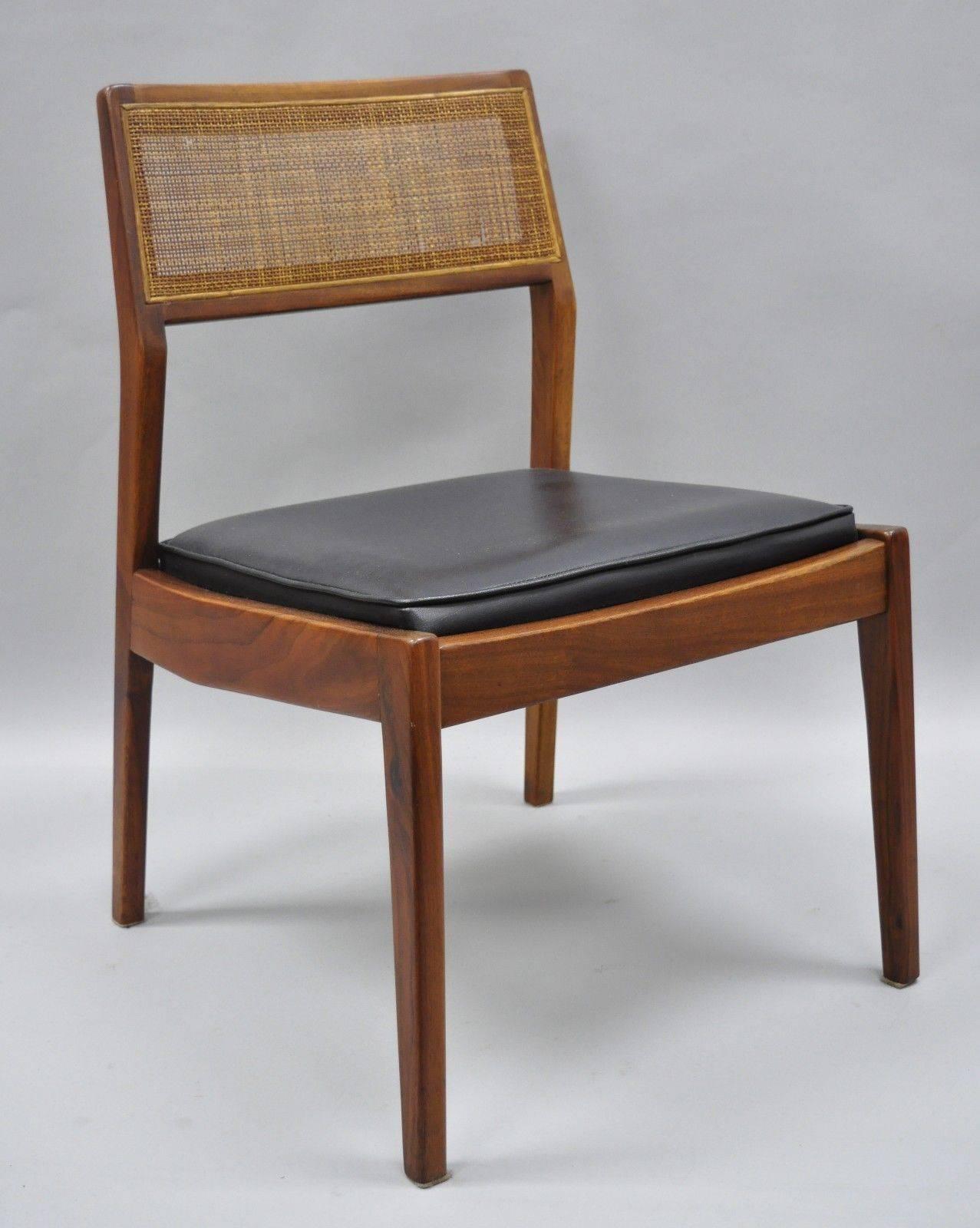 Set of six Jens Risom walnut and cane back dining chairs. Set includes five side chairs, one armchair, black vinyl seats, cane backs, solid wood construction, beautiful wood grain, sleek sculptural form, mid-20th century. 
Measurements: 
Armchair