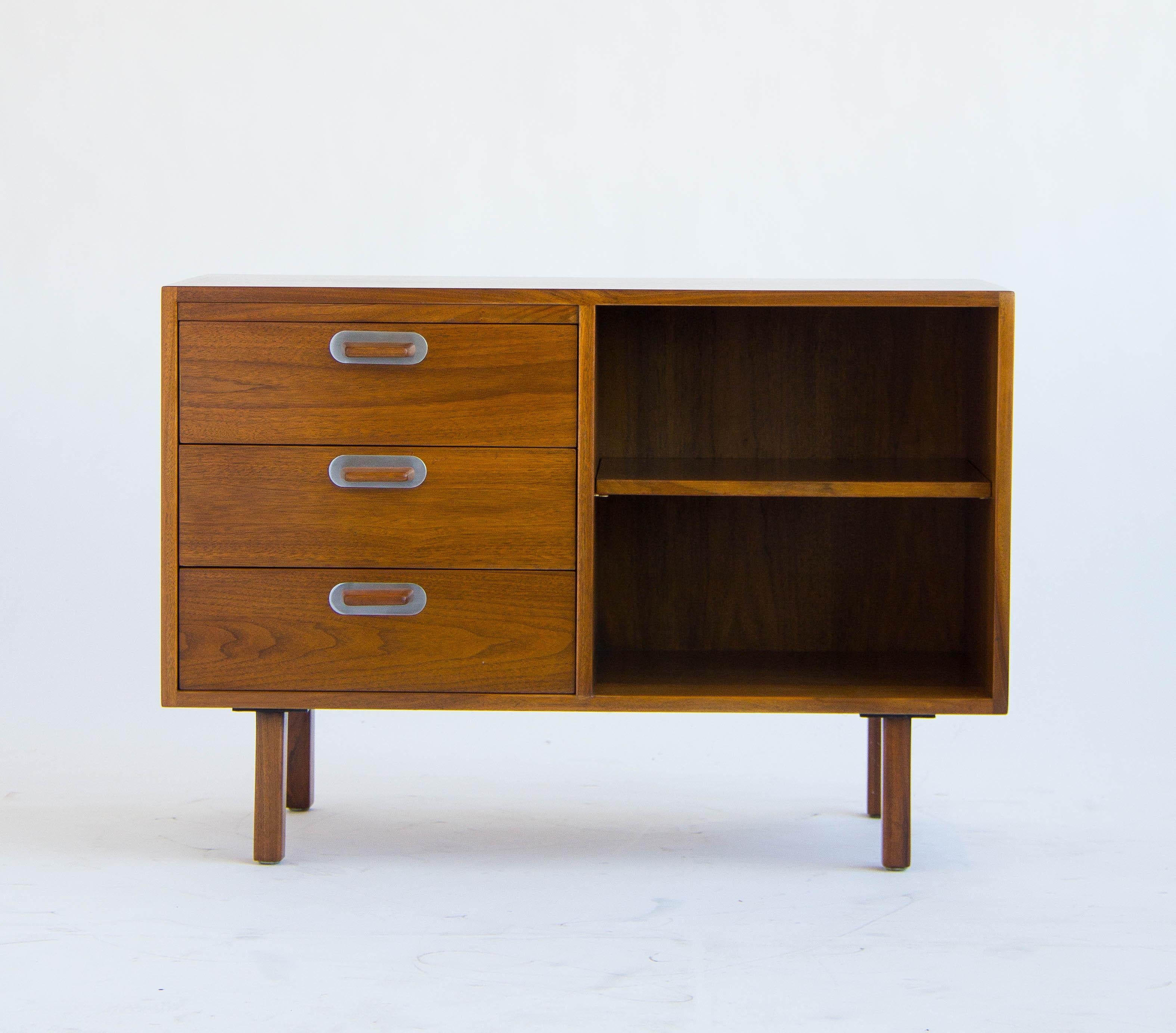 This compact credenza by Jens Risom, is made of solid walnut and finished with polished aluminum details. Left side has three drawers and the right side is open with two shelves. The finished back allows for placement anywhere. Retains Jens Risom