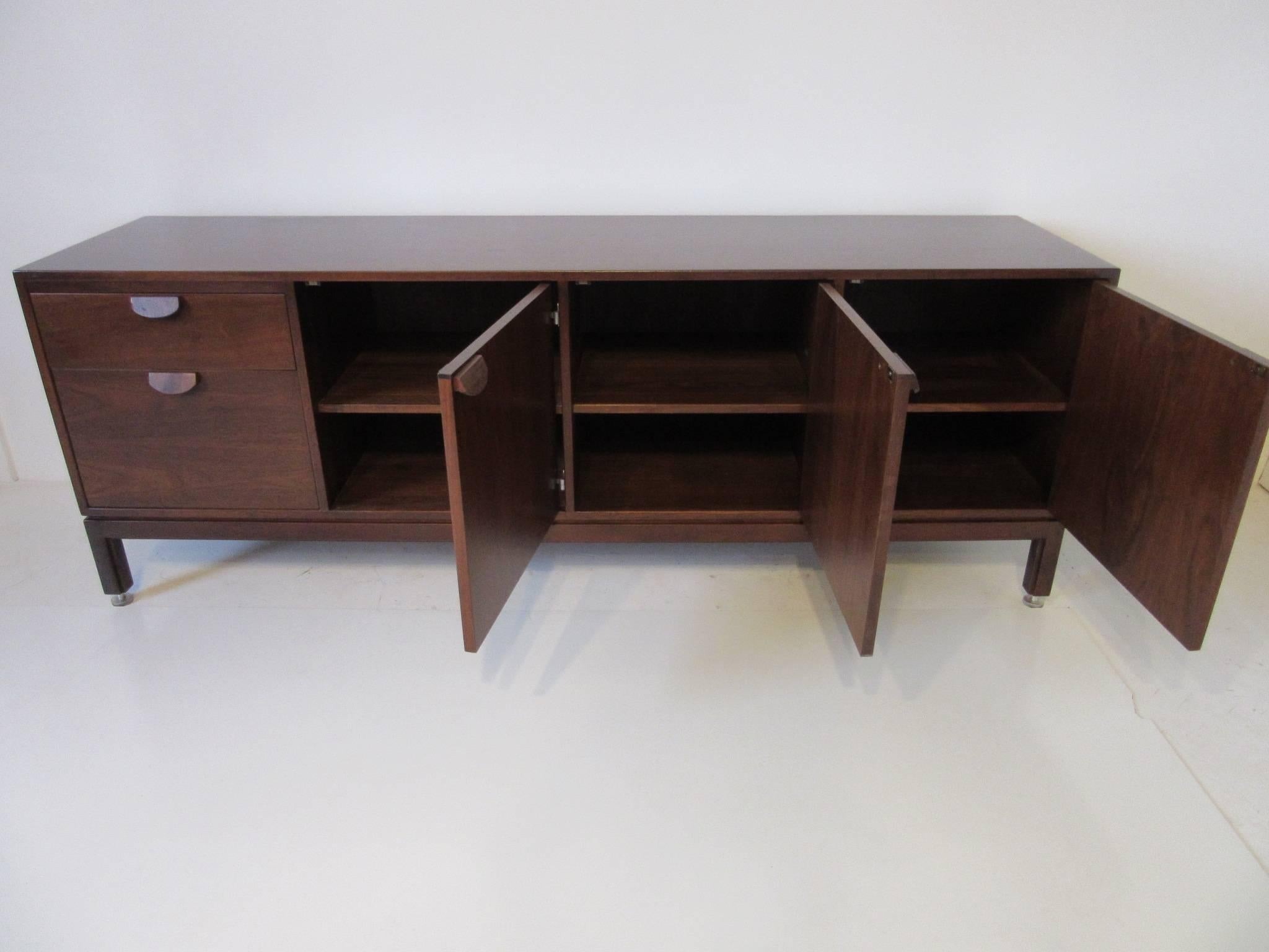 A dark walnut two-drawer and three door credenza with matching wooden pulls, stainless hinges and stainless adjustable foot pads. Finished to the backside with the same well grained walnut the inside contains storage and adjustable shelving. Finely