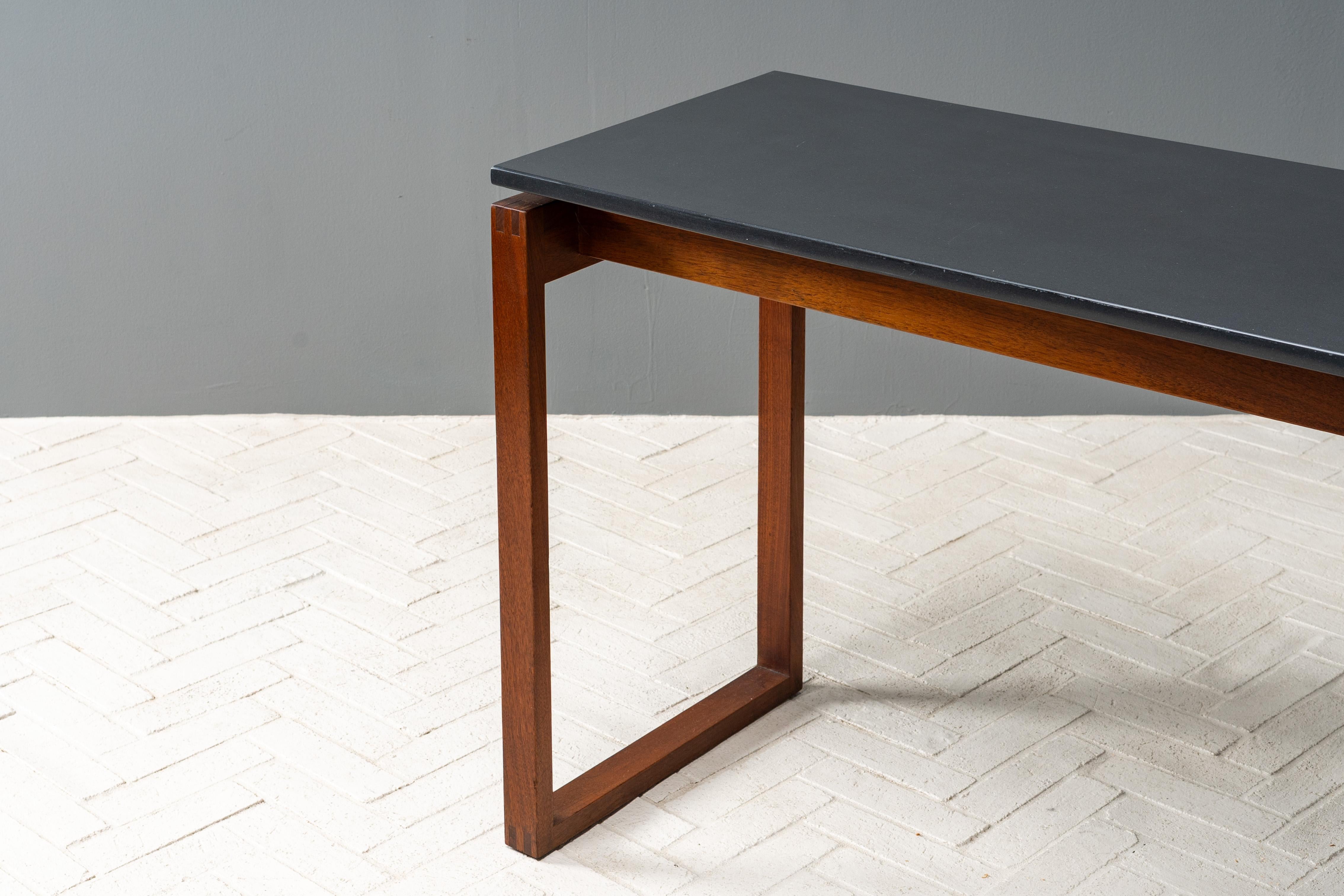 USA, circa anni '60. Un'attraente consolle rettangolare di Jens Risom per Jens Risom Design. Presenta un piano in ardesia fluttuante sostenuto da gambe a slitta in noce massiccio. Le giunzioni a pettine visibili e le barelle incassate aggiungono