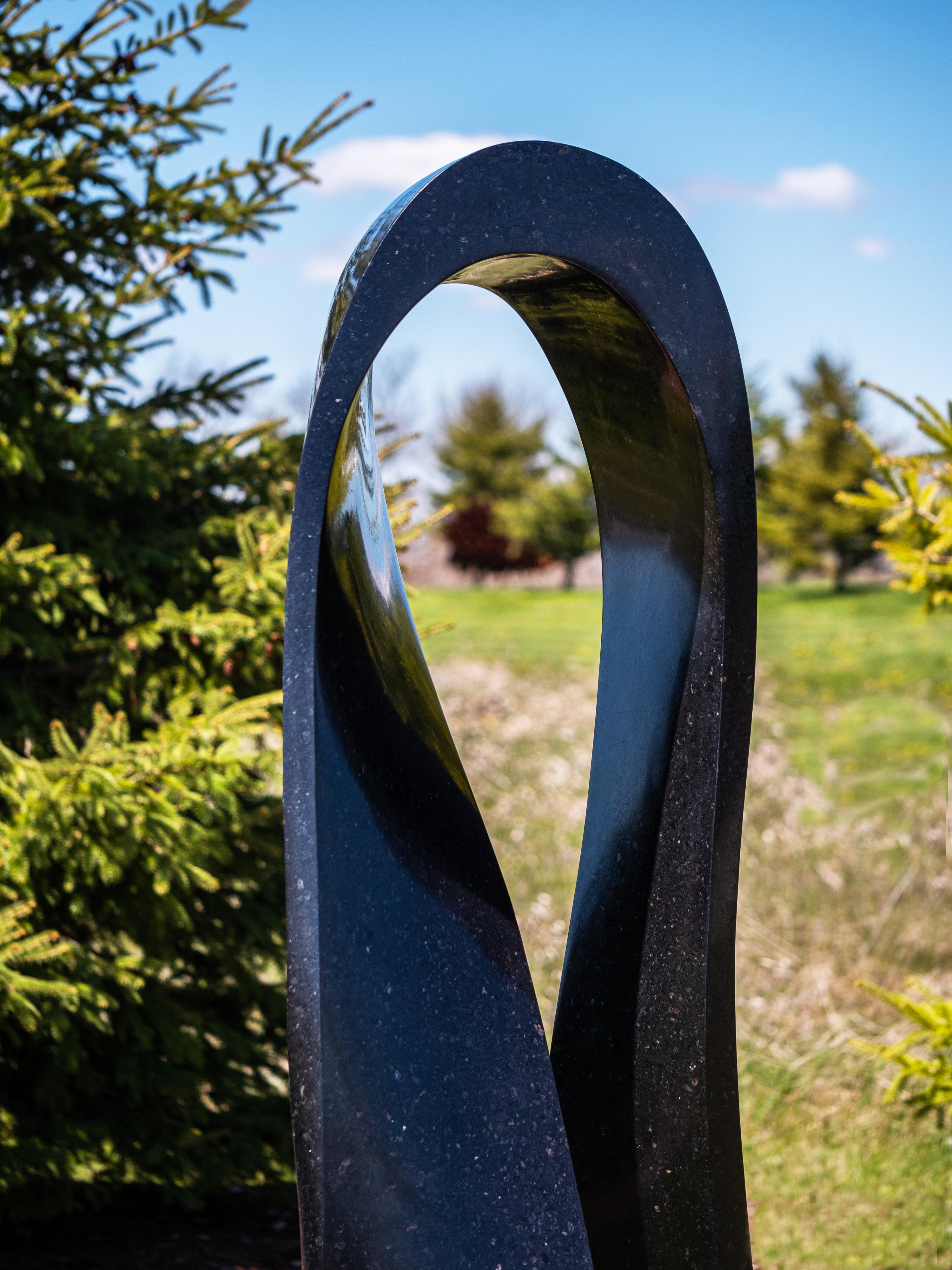 Smooth surfaced, black granite has been engineered by Jeremy Guy into an elegant outdoor sculpture in the form of a mobius strip. Discovered by the German mathematician August Ferdinand Möbius, a Möbius strip is a surface with only one side and only