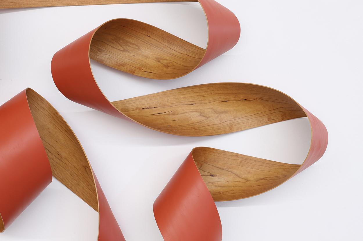 Abstract bent cherry wood sculpture painted with a burnt orange paint on one side. 