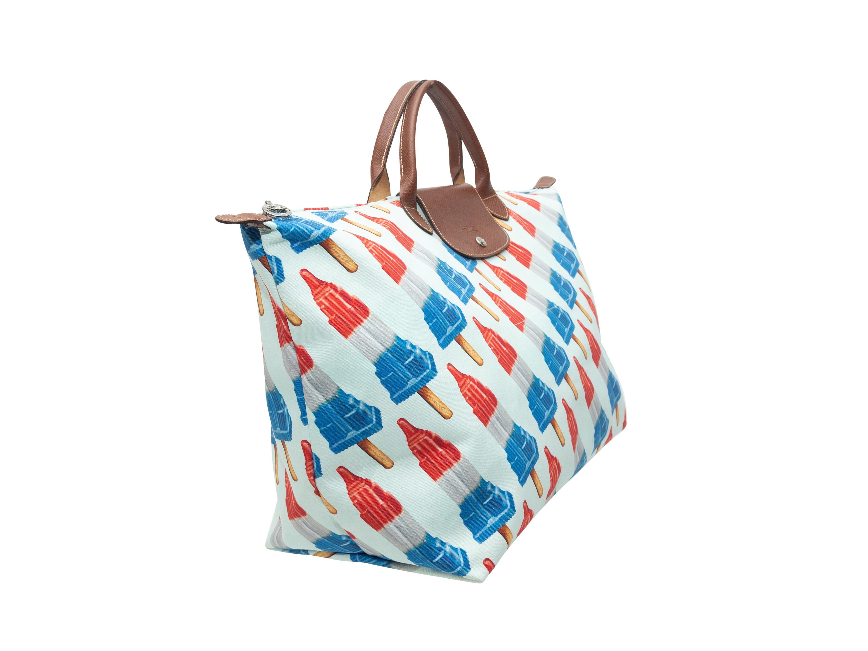 Product details: White and multicolor Empire State Building popsicle print tote bag by Jeremy Scott x Longchamp. Brown leather handles. Zip closure at top. 17