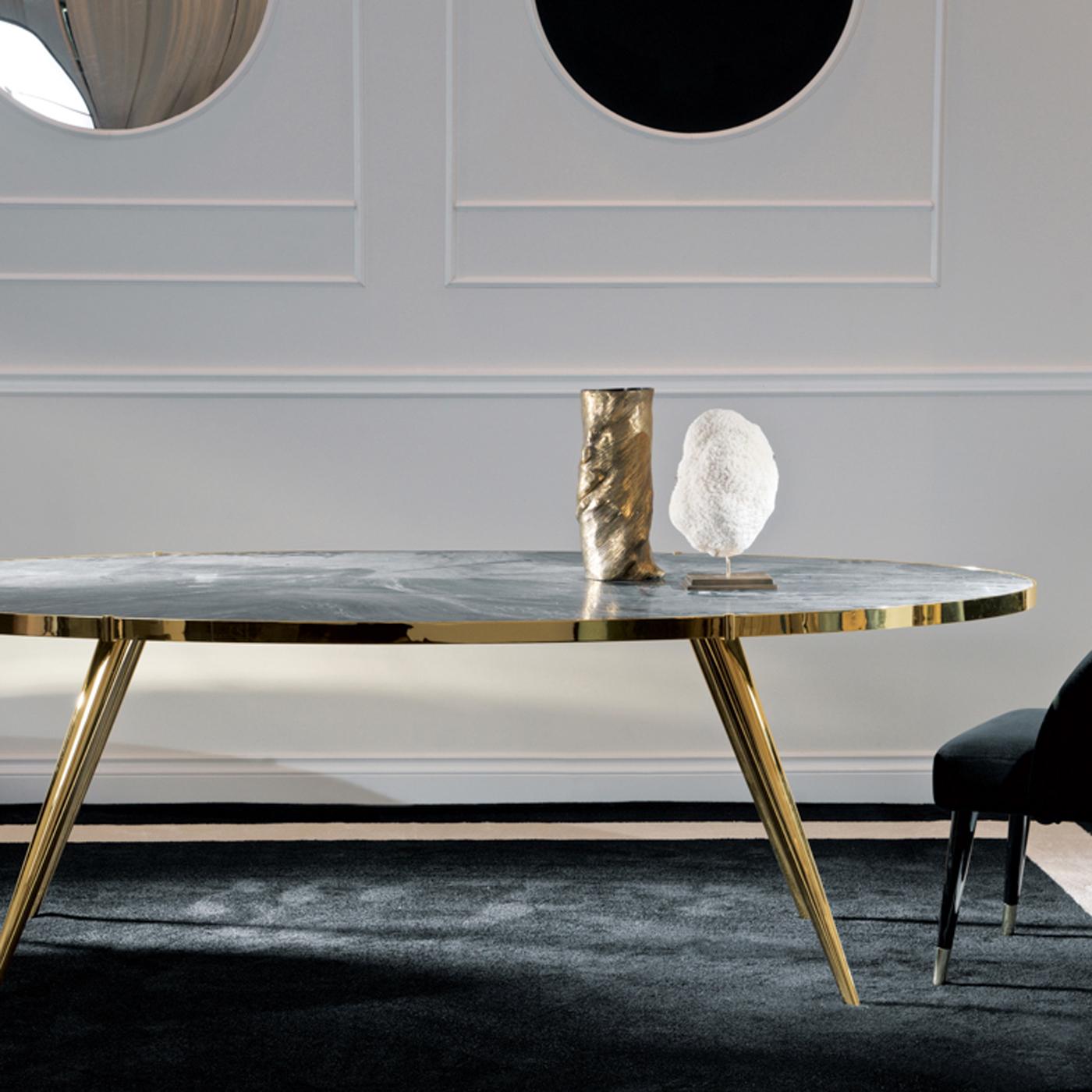Part of the Jerome Collection, this dining table boasts tapered and slanted legs that give it a mid-century allure, supporting an oval top. Sophisticated and timeless, this piece is made of metal with a glossy brass finish, included the mounting of