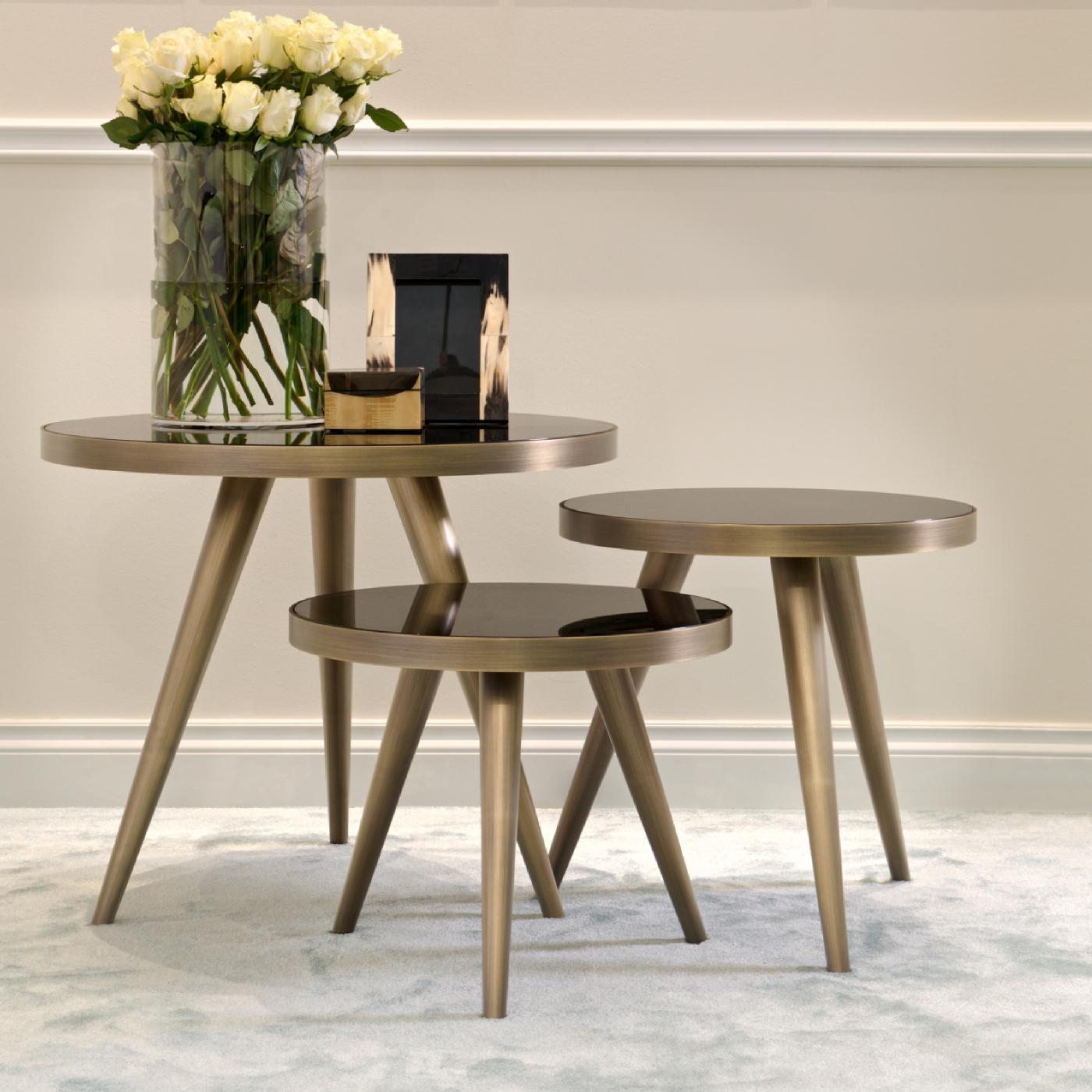 This precious set of three side tables is part of the Jerome Collection, inspired by the charm of midcentury design, crafted with exquisite craftsmanship, and using high-quality materials. Each piece features a round top in glass with a black